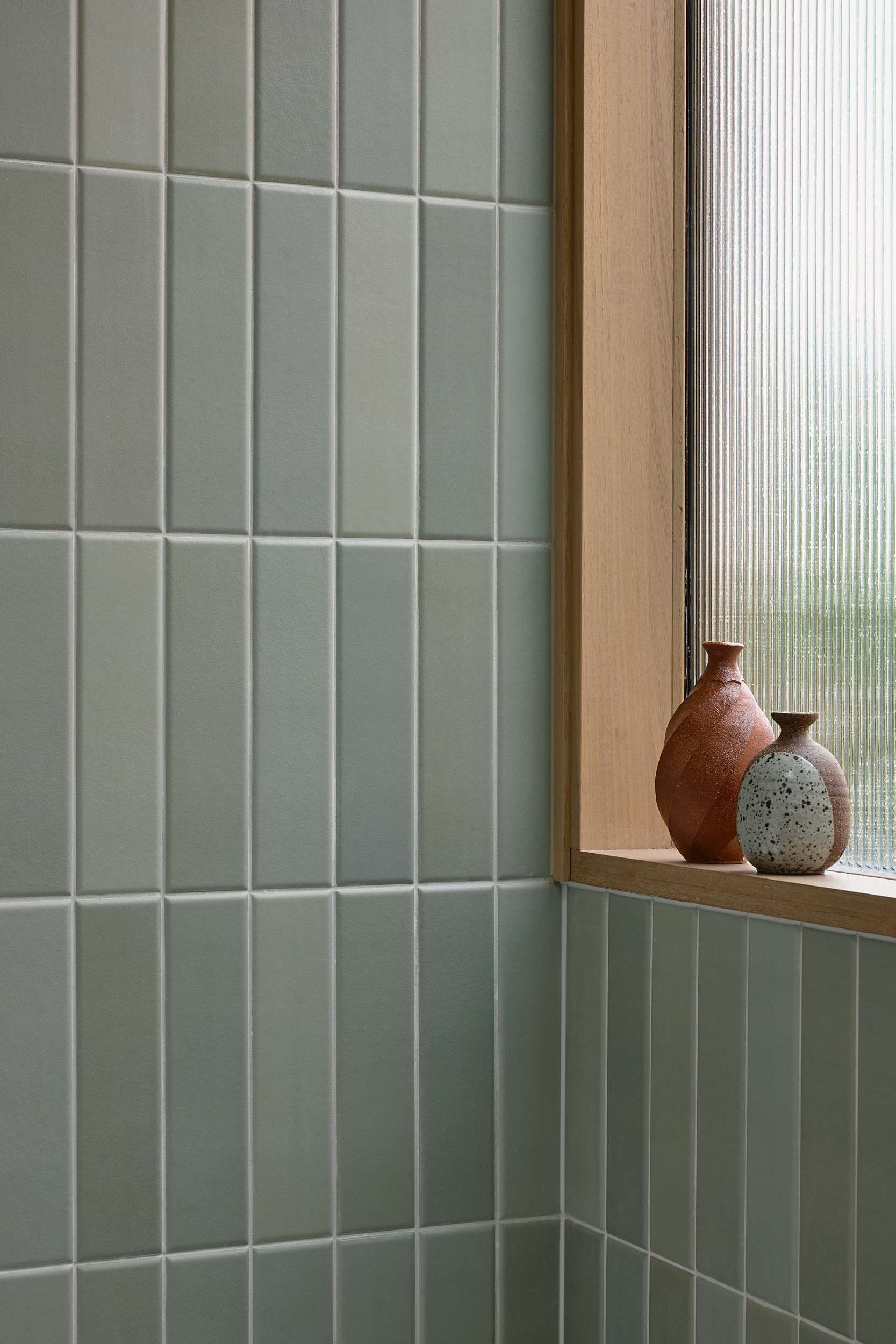 Home Pavilion by MRTN Architects. Close up detail short of timber window frame with fluted glass inset, clay pots on frame and tiled wall in varying shades of sage green. 