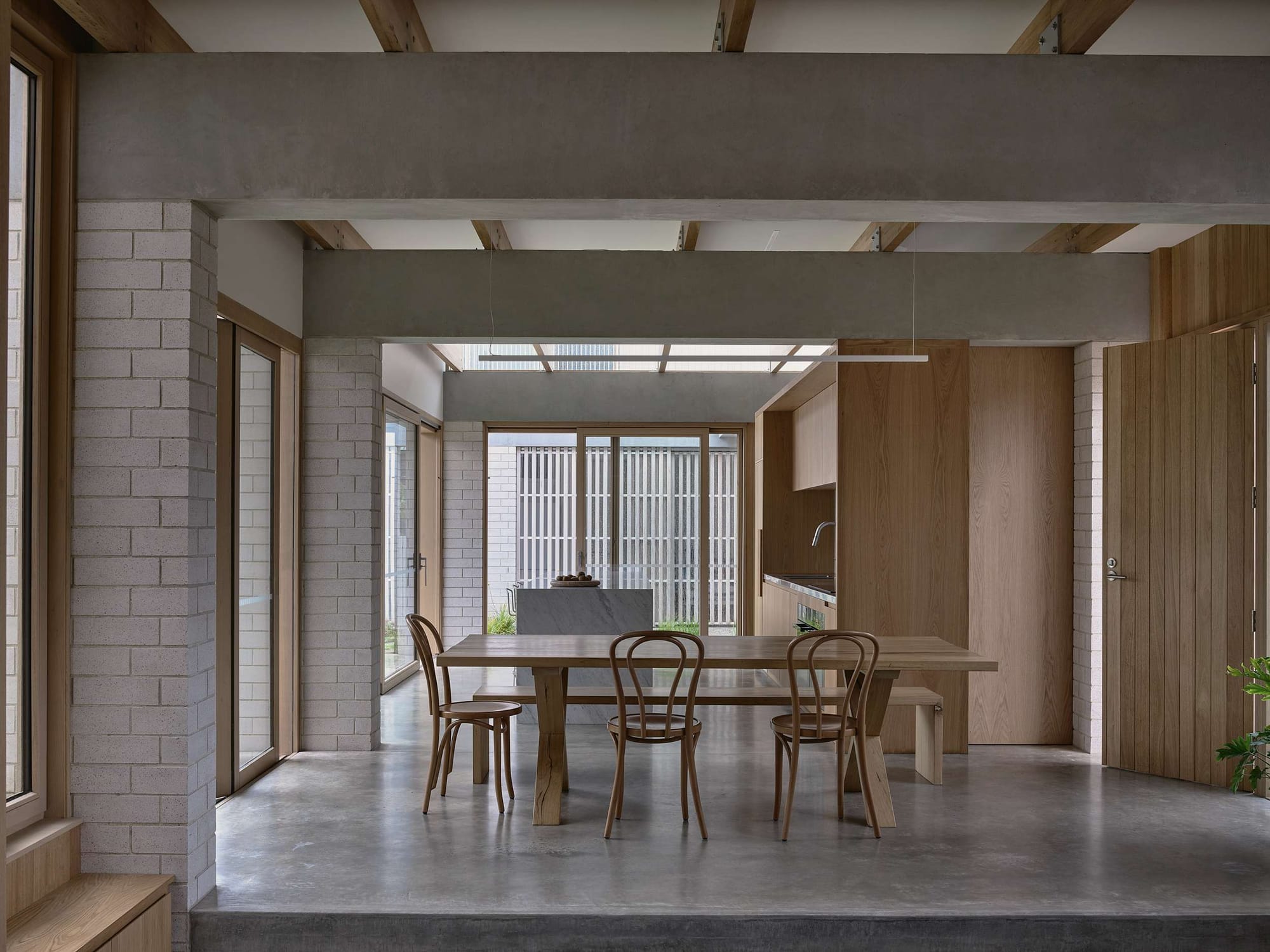 Home Pavilion by MRTN Architects. Timber dining table and chairs in open plan space with concrete floors, exposed concrete beans, brick pillars and timber doors and windows. 