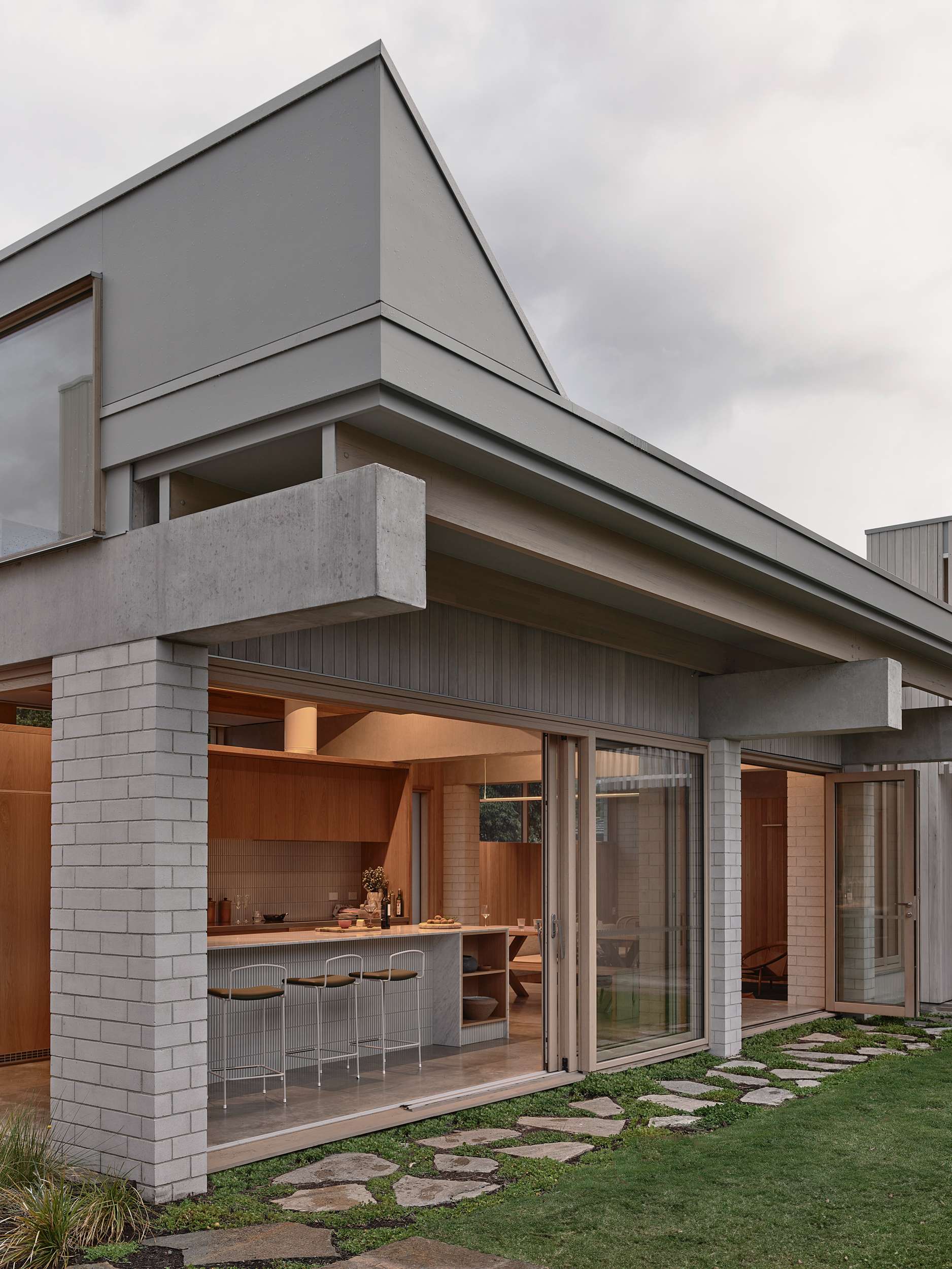 Home Pavilion by MRTN Architects. Corner of home with brick pillars, concrete beams, sliding timber framed glass doors and windows, framing kitchen interior. 