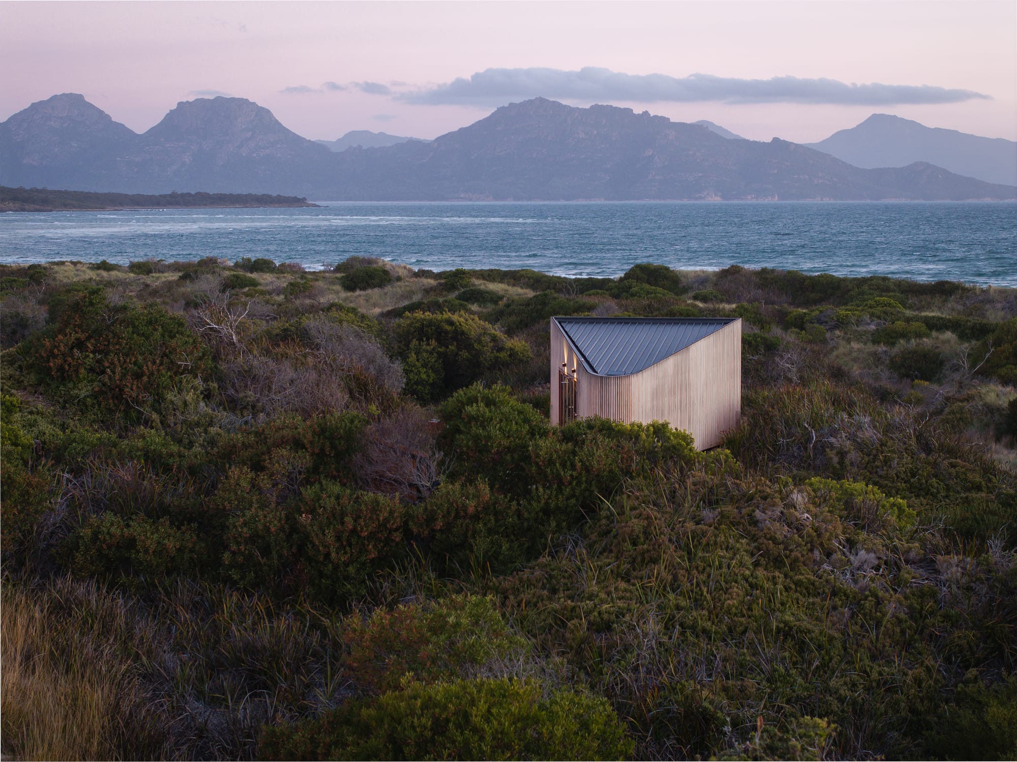 A dusk shot showing Studio Tasmania sitting in its coastal landscape with the ocean and mountains in the background.