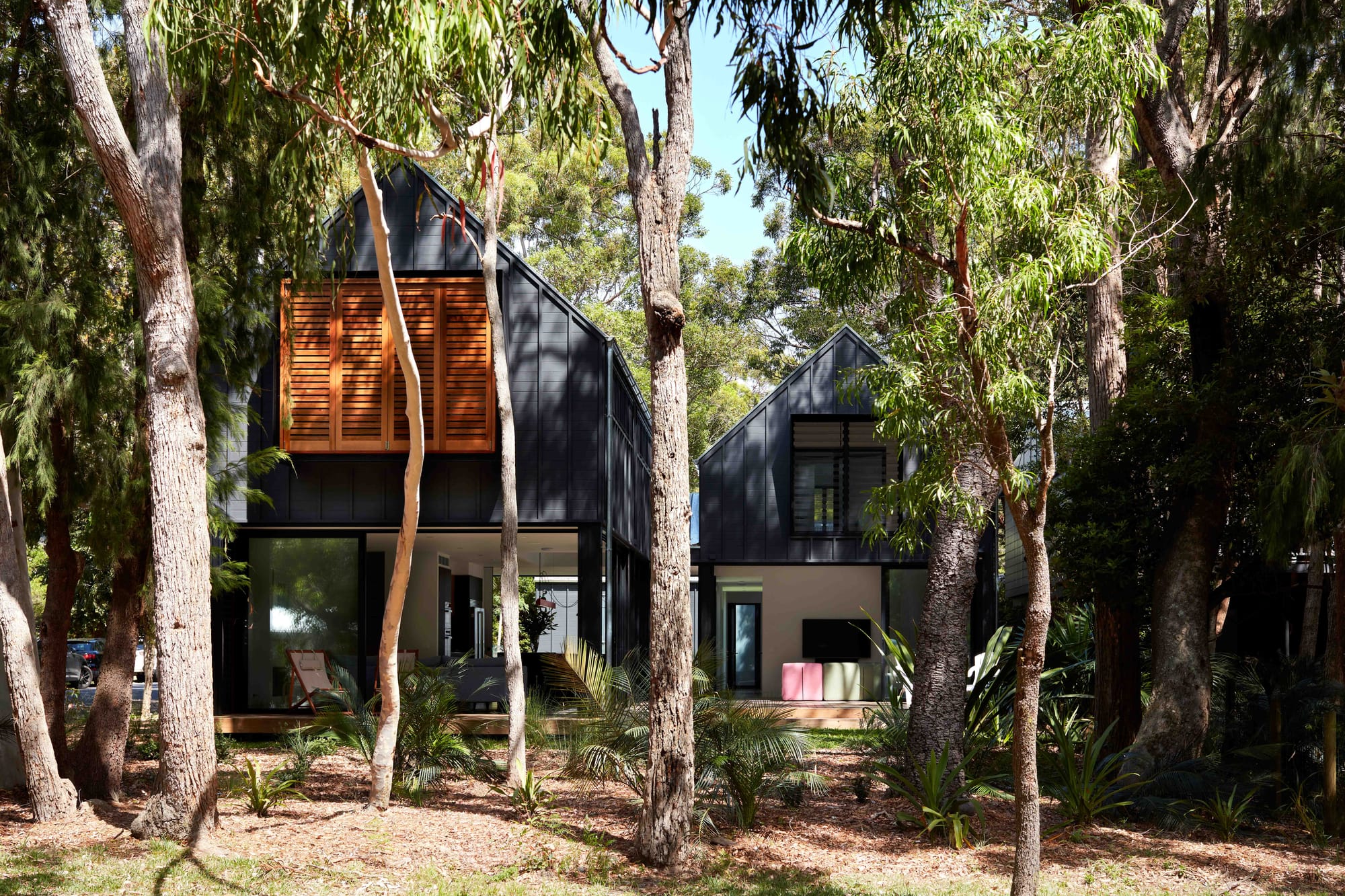 Pearl Beach II by COSO Architecture. Home in the forrest. Black-framed home with wooden shutters.