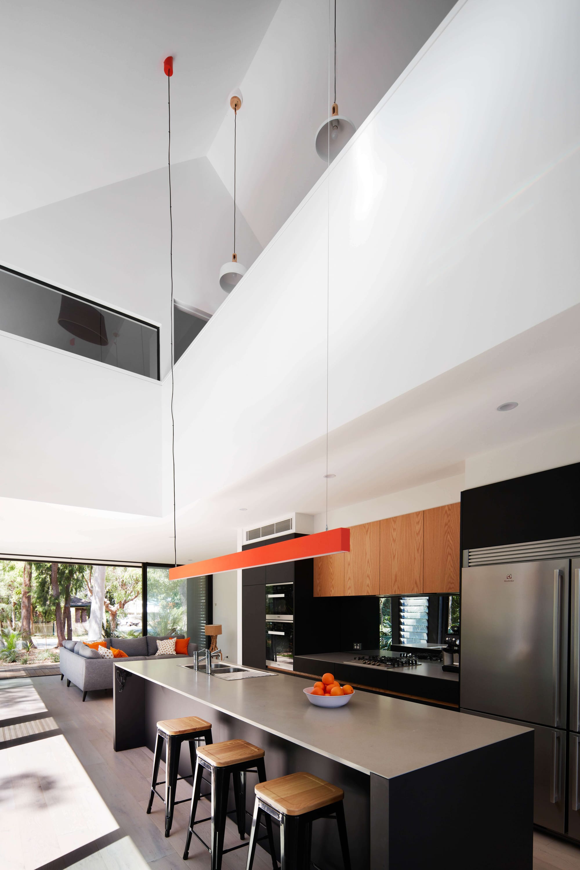 Pearl Beach II by COSO Architecture. Kitchen with large windows. Grey kitchen island with bar stools. Wooden cabinets and grey fridge.