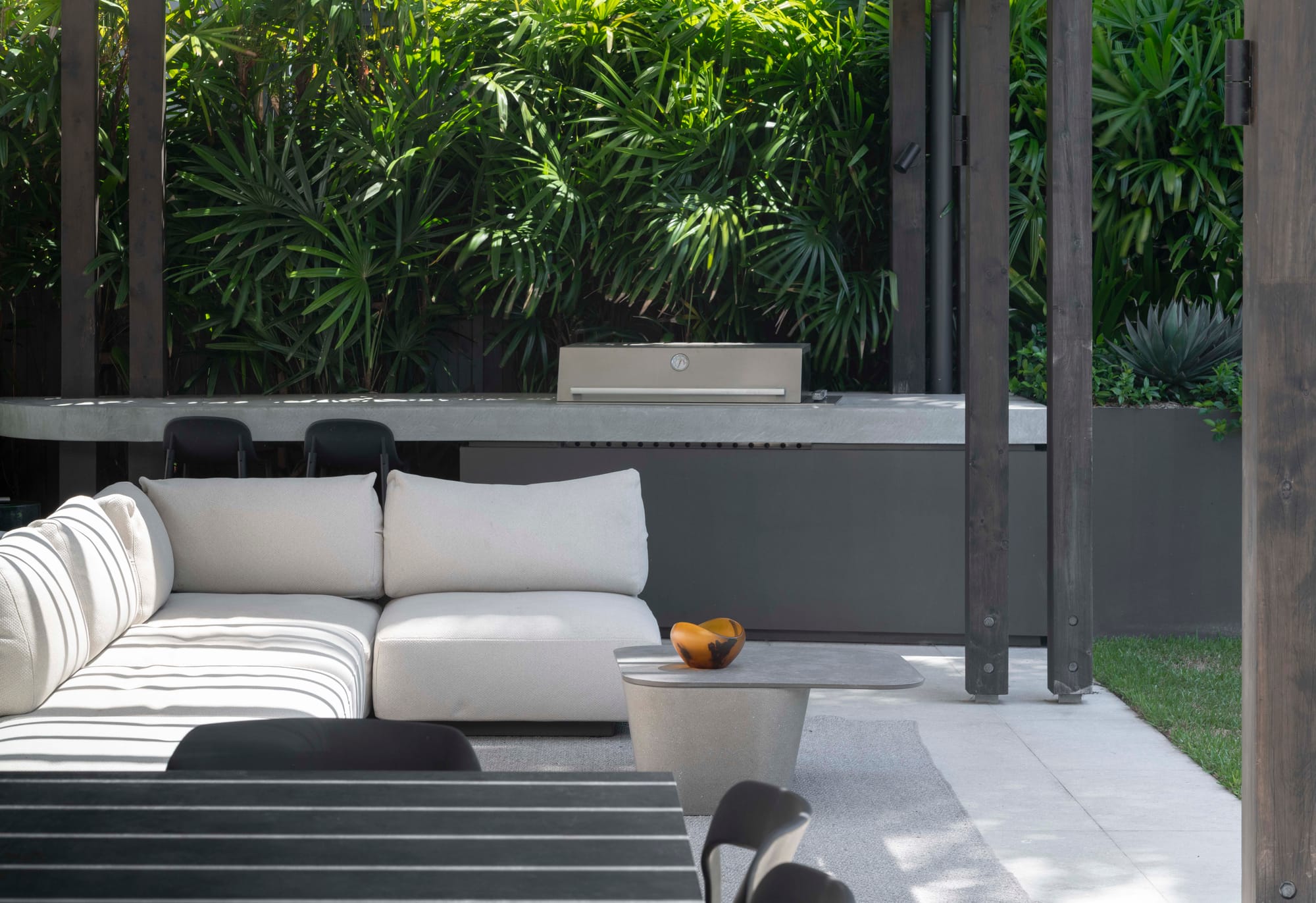 Outdoor lounging area with cream daybed and table with built-in barbeque.