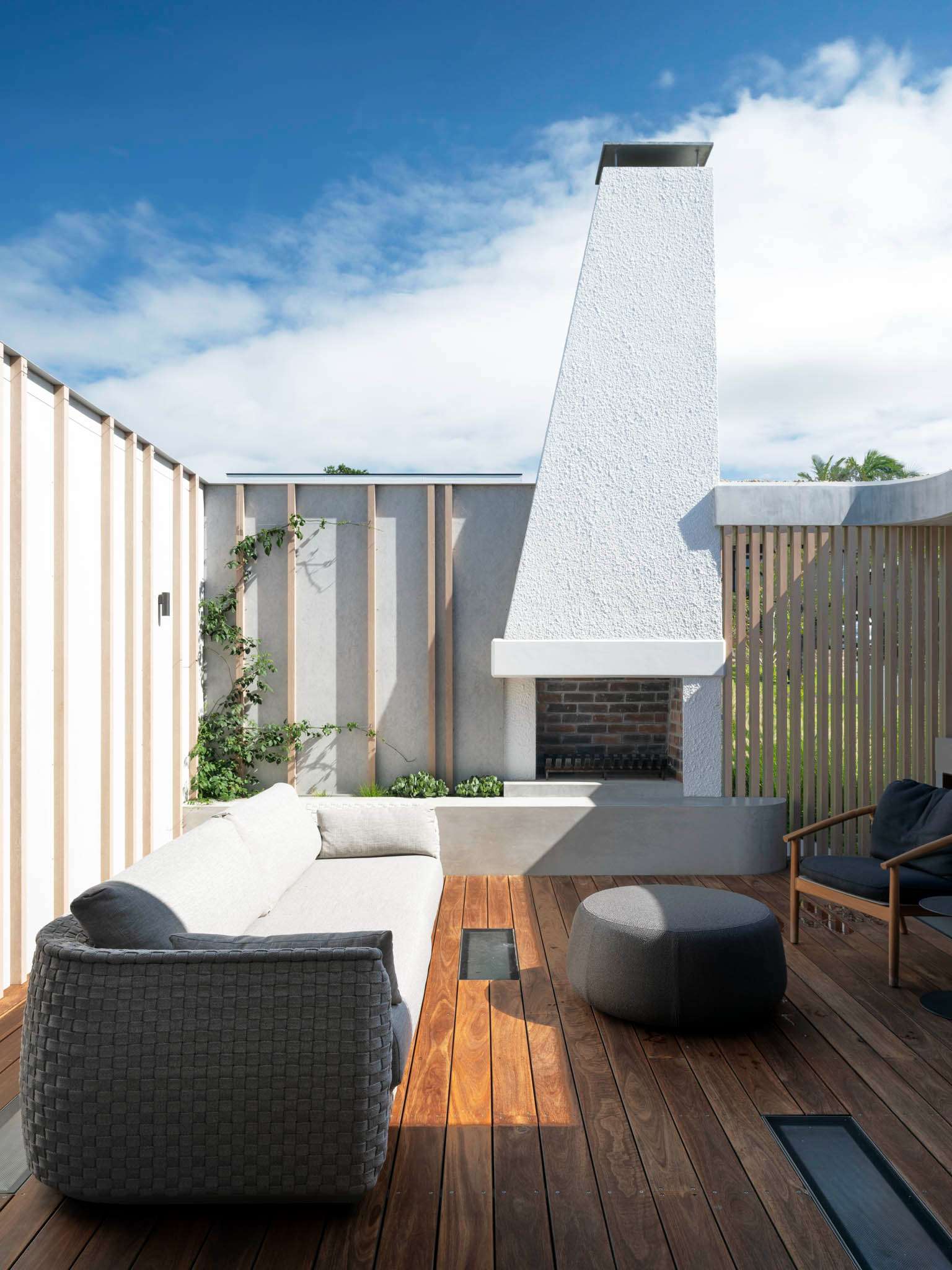 Sirius by Castlepeake Architects. Photographed by Tom Fergurson. Outdoor lounge area with fireplace. Wooden flooring with white chimey. Grey chairs.