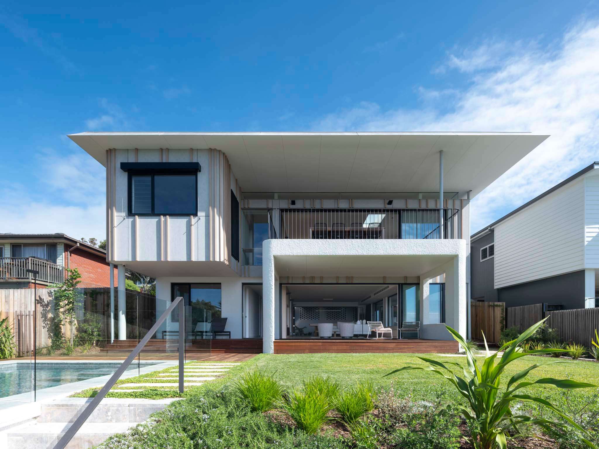 Sirius by Castlepeake Architects. Photographed by Tom Fergurson. Backyard with pool. Outdoor area with lounge chairs. White exterior house.