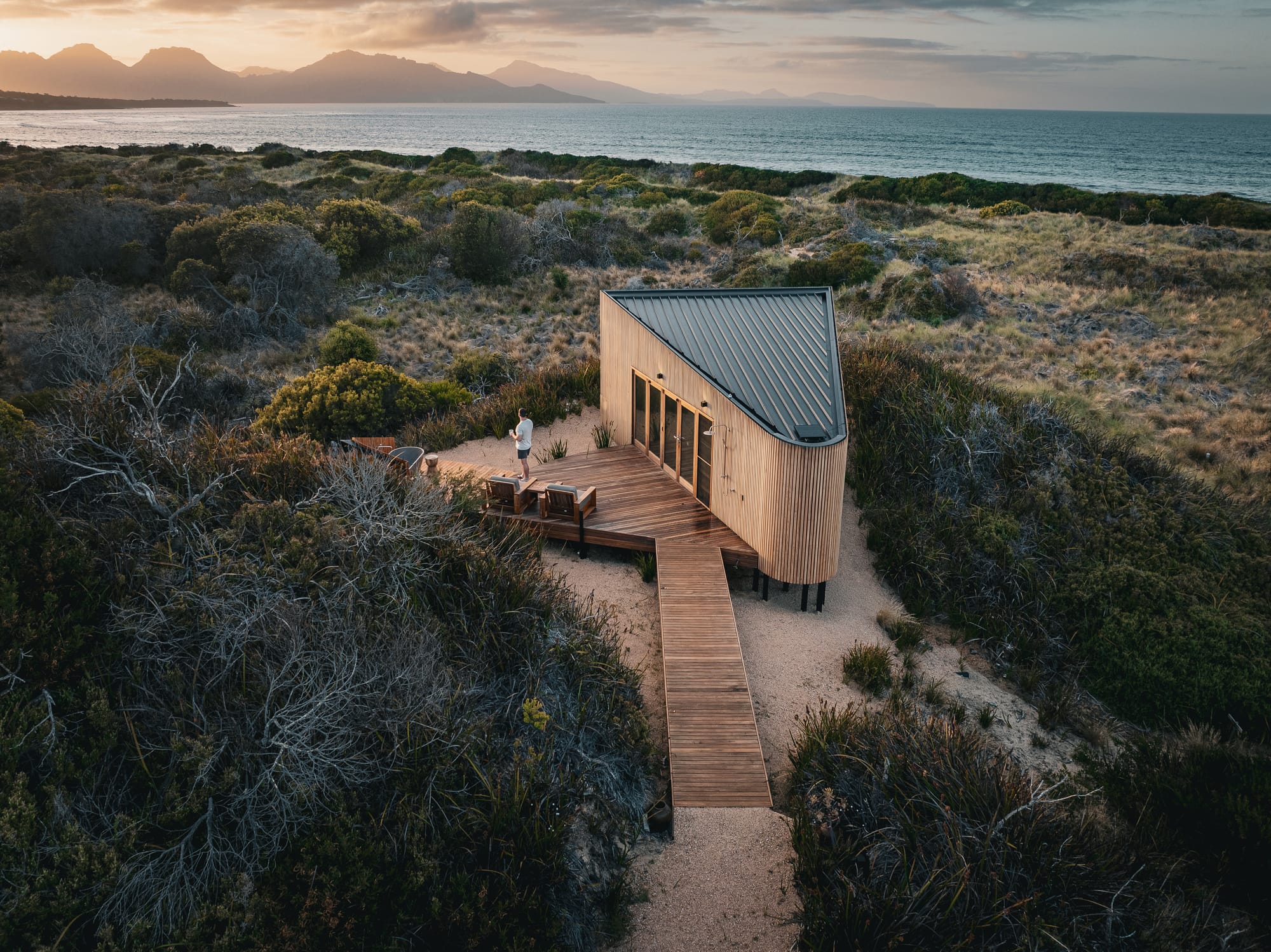 A birds eye view of Studio Tasmania showing the timber cabin and the coastal scrubland that surrounds and panoramic ocean views.