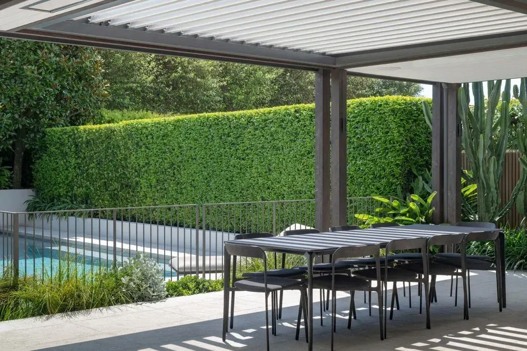Grey outdoor dining set in shade structure with grey fencing and pool.