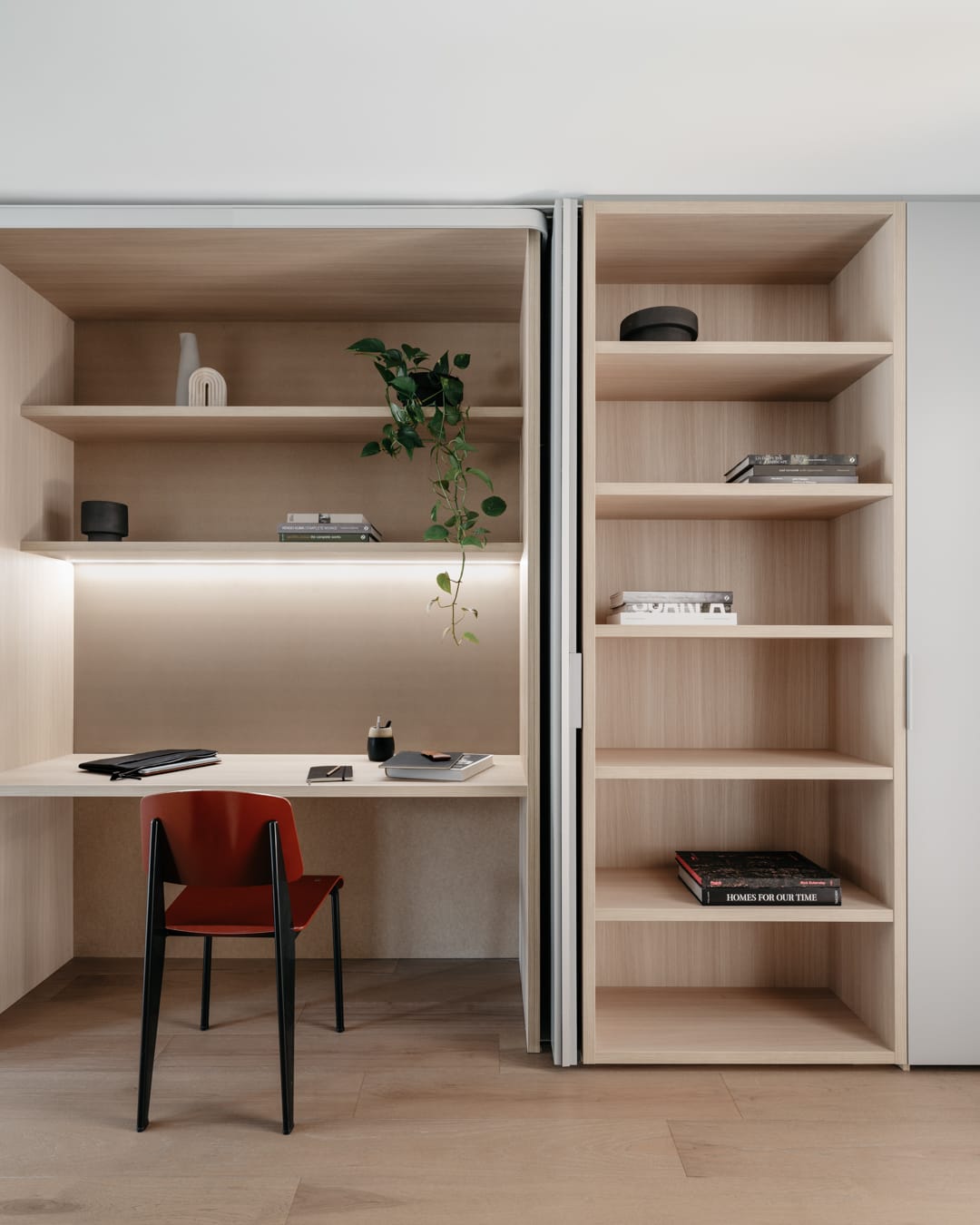 Custom timber shelving and desk nook with integrated lighting and a red chair, showcasing detailed residential joinery.