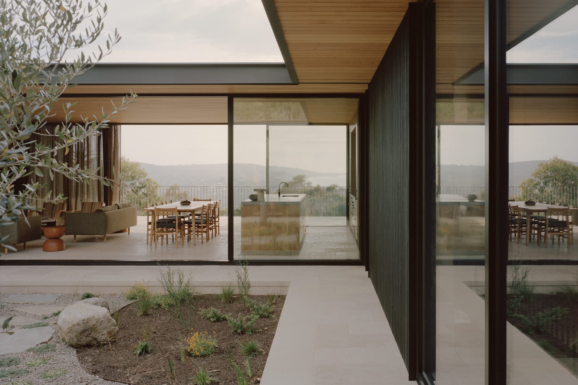 Modern home with large sliding glass doors opening to an outdoor terrace, framing views of a coastal landscape.