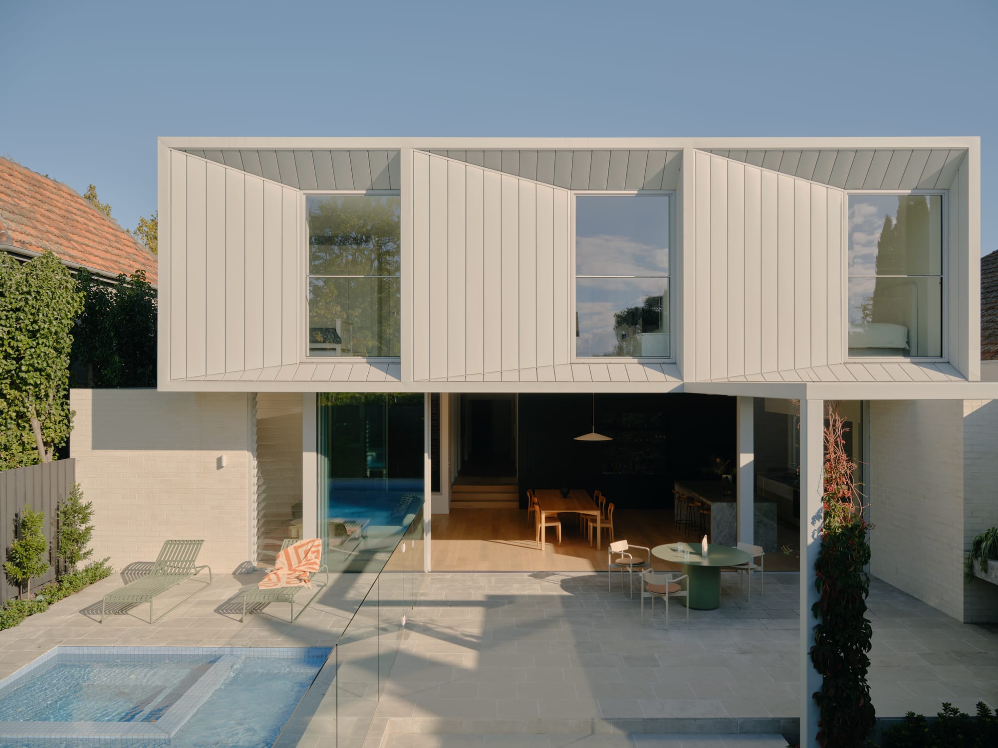 Modern home with sculptural upper-level windows overlooking a courtyard with a pool and outdoor living area.