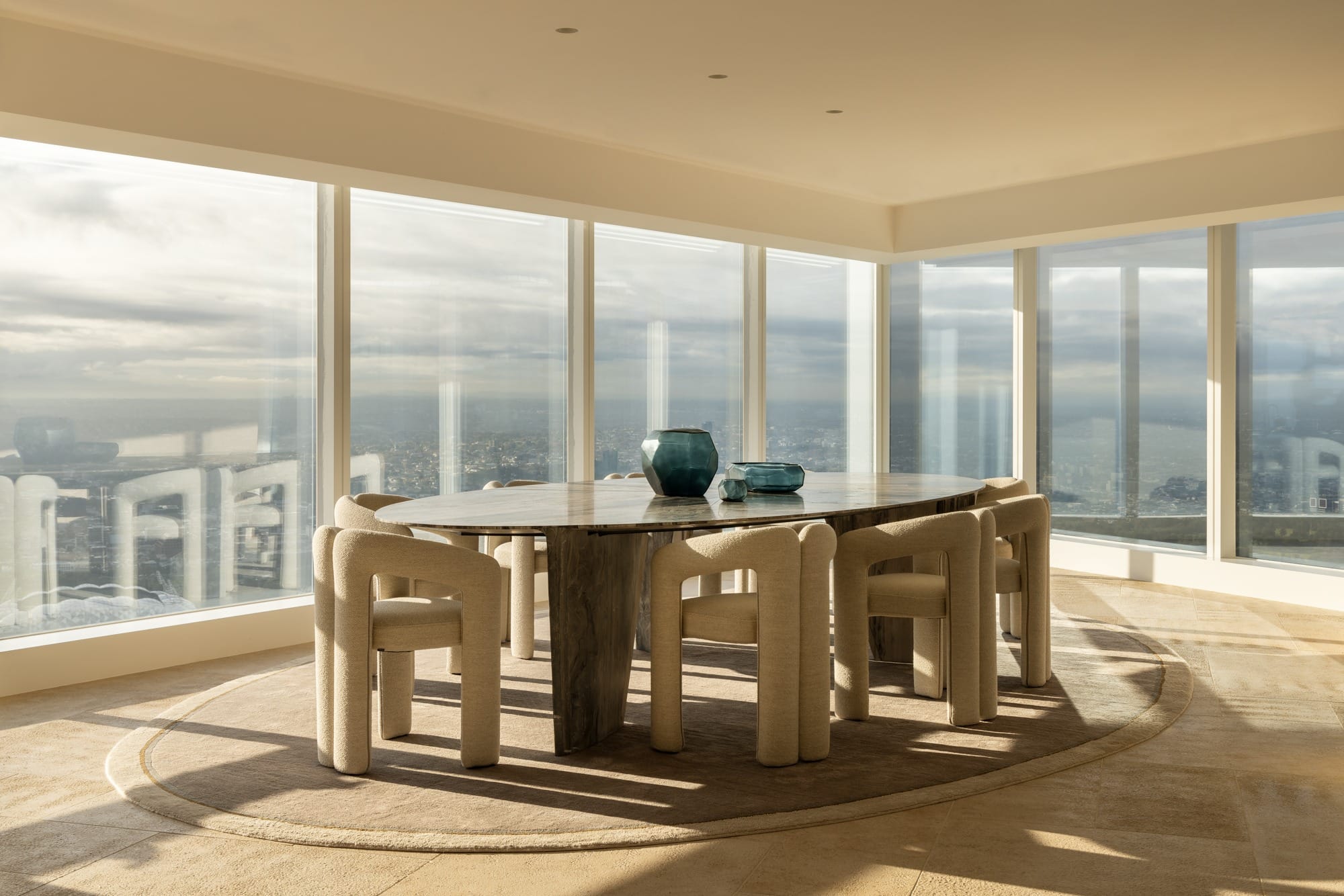 Modern penthouse dining room with round table, upholstered chairs and panoramic city views through full-height glazing
