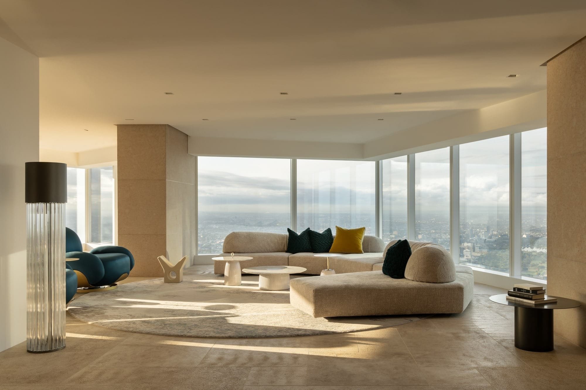 Luxury penthouse living room with curved sofa, neutral palette and floor-to-ceiling windows overlooking Melbourne skyline