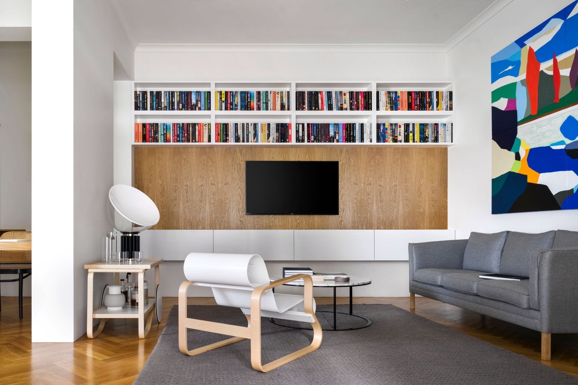 Modern living room with built-in bookshelf wall, timber panelled TV unit and minimalist furniture