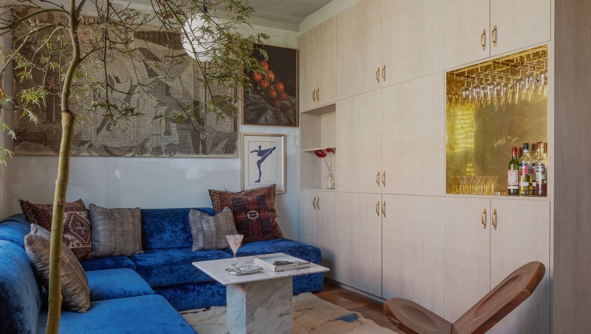 Compact living room with blue velvet sofa, marble table and built-in bar with brass detailing