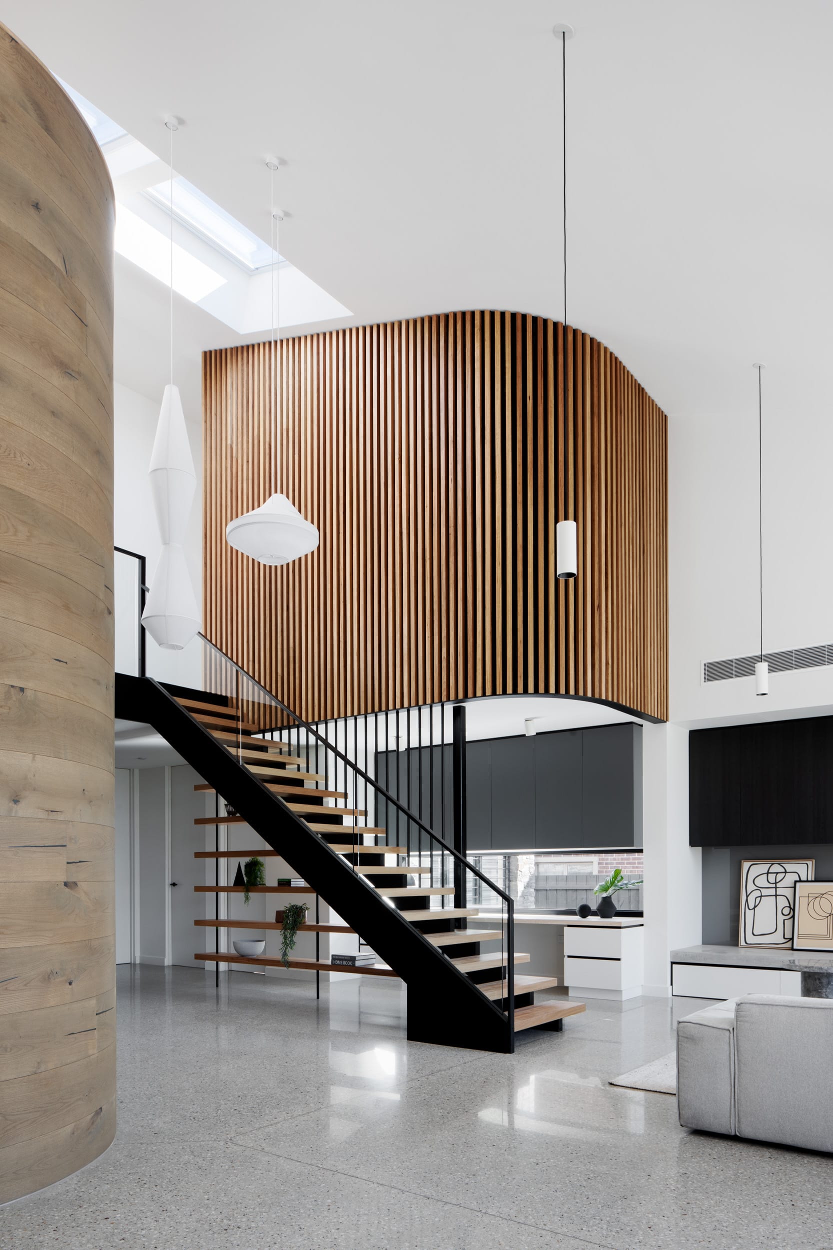 Modern interior featuring a floating staircase, curved timber batten wall, and skylit open-plan living space.