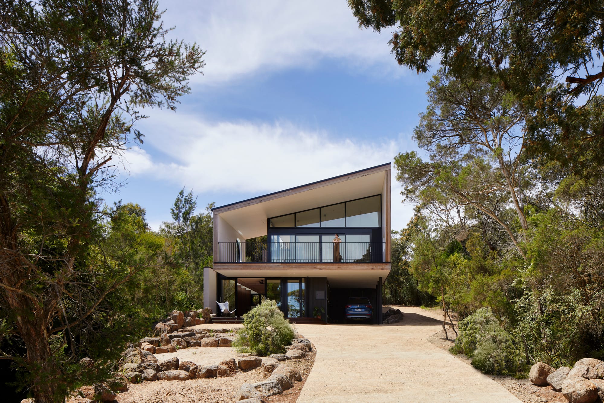 Modern elevated house set within a natural bush landscape, with large windows and a balcony overlooking the site.