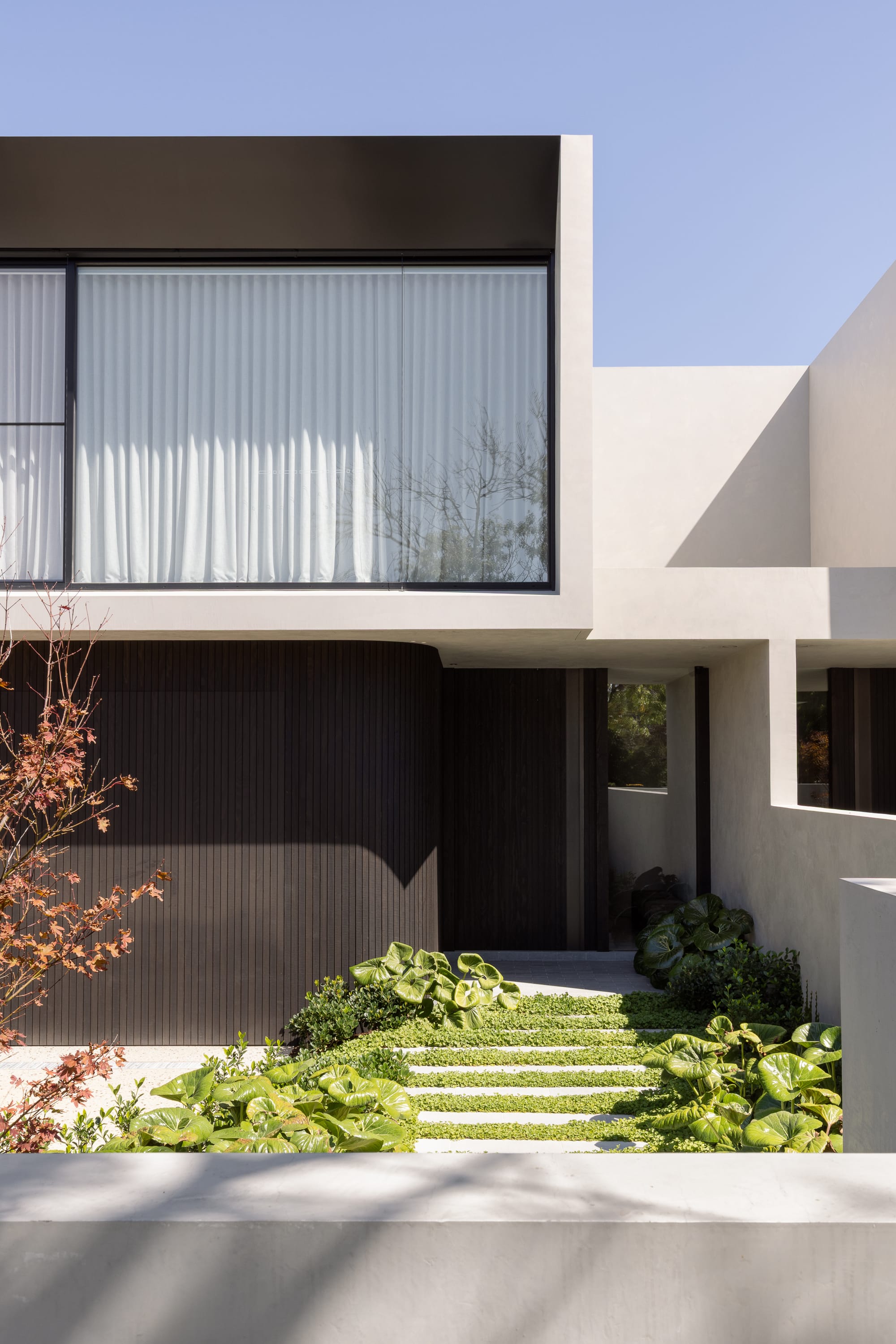 Minimalist white house facade with strong geometric forms, large window, and landscaped entry courtyard.