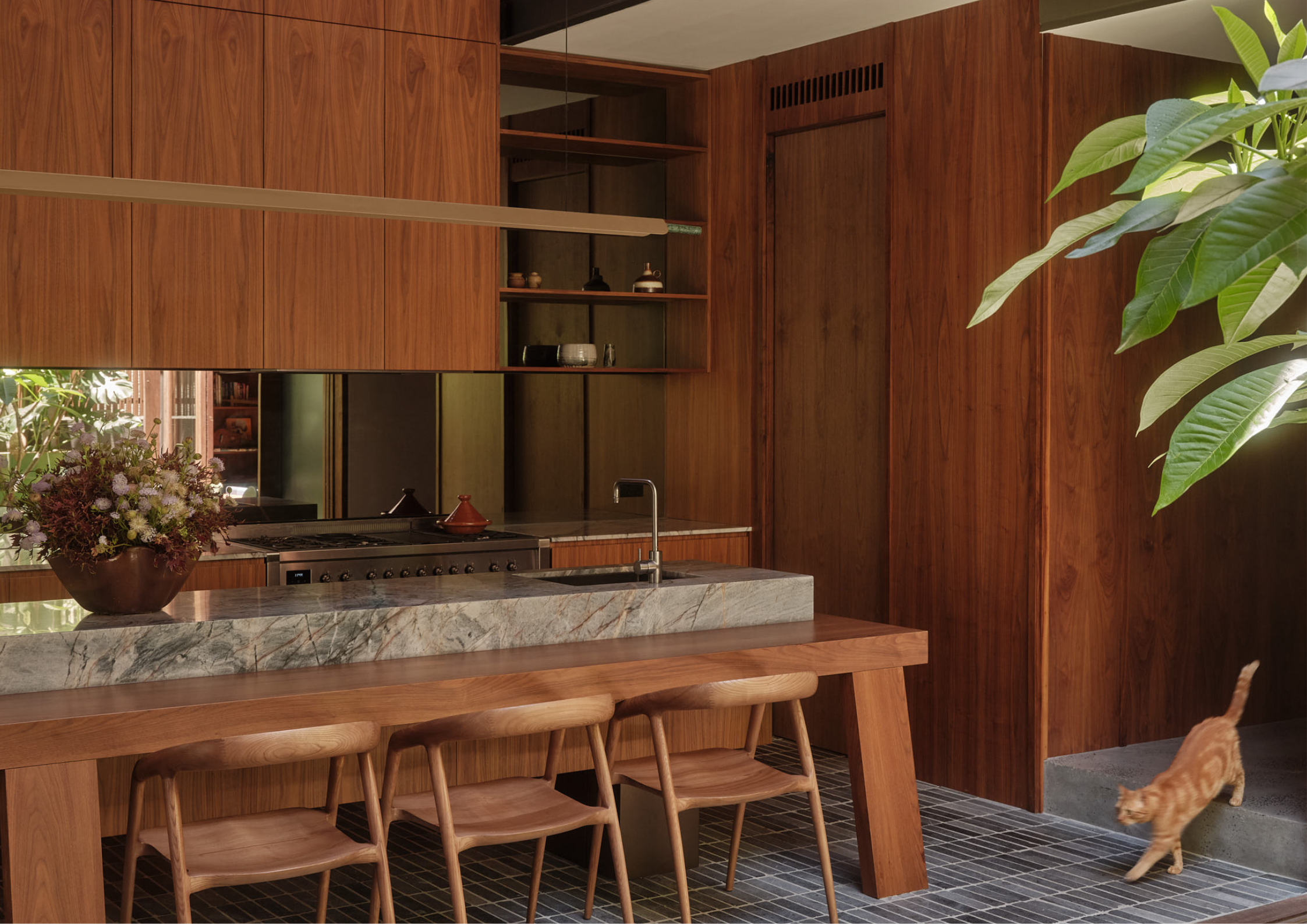 Rich timber kitchen interior featuring marble island bench, custom joinery, and warm natural light filtering through the space.