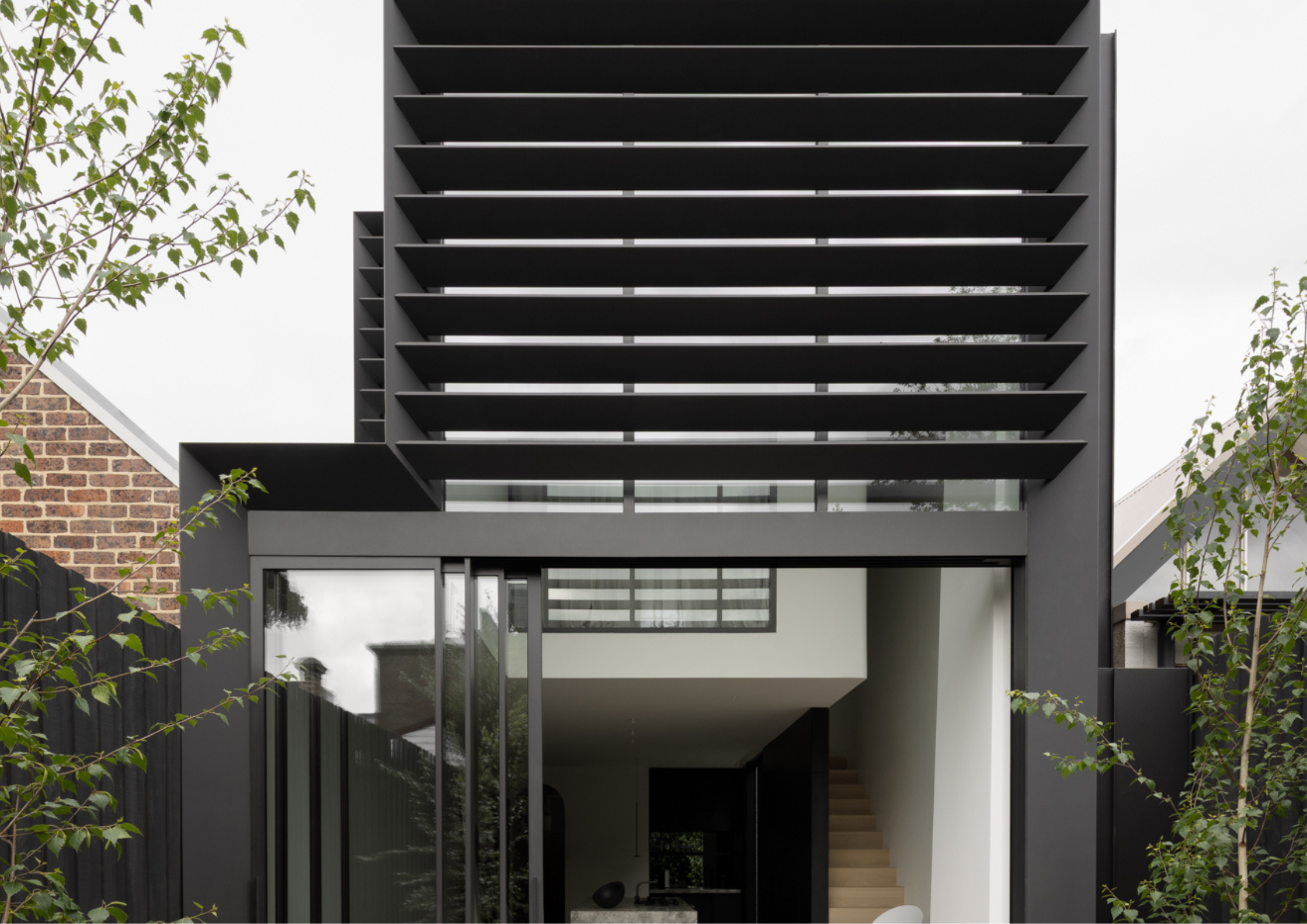 Modern façade with black horizontal louvres above a glass entry and minimalist landscaping.