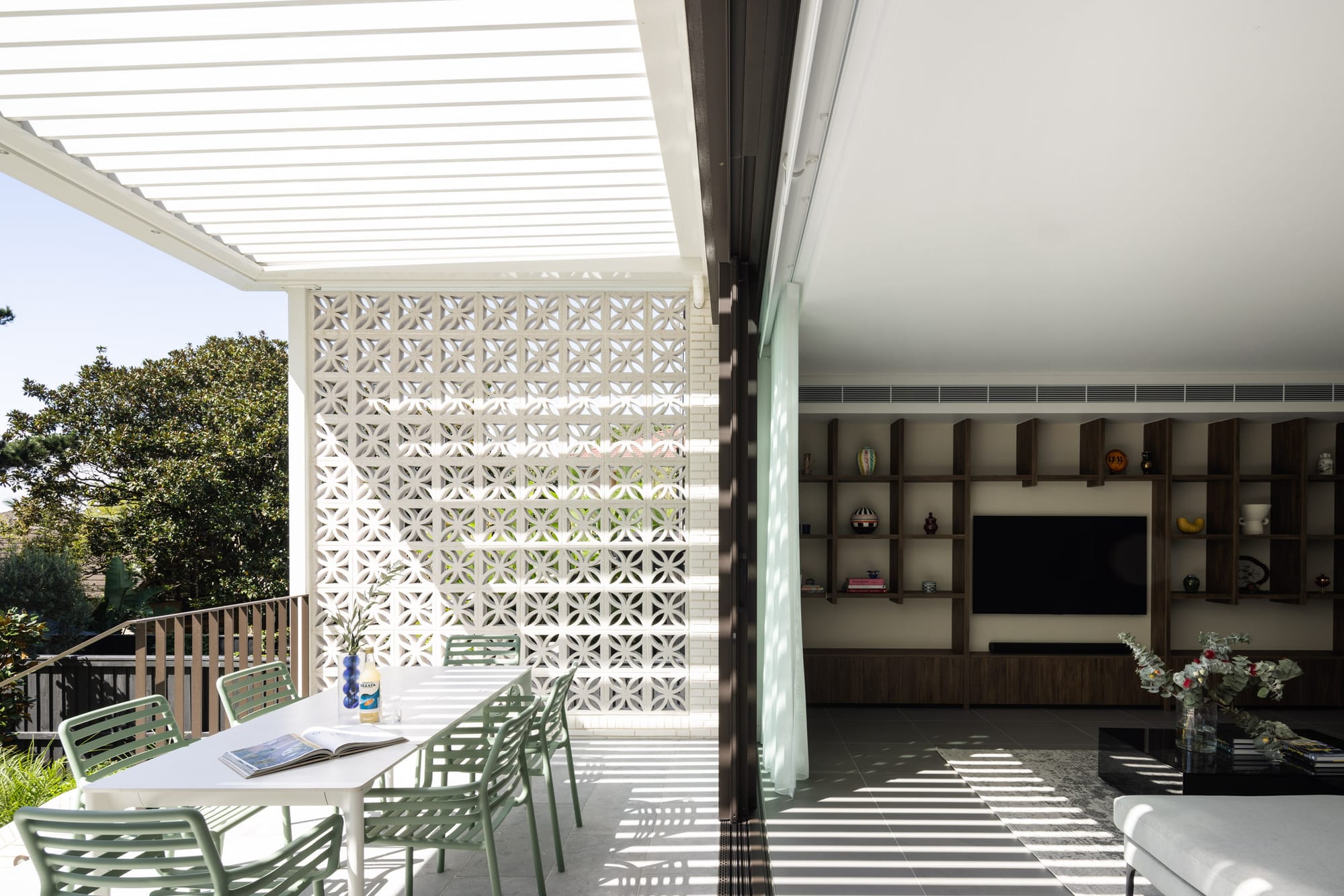 Indoor-outdoor living space with breeze block screening, shaded terrace dining, and custom timber shelving.