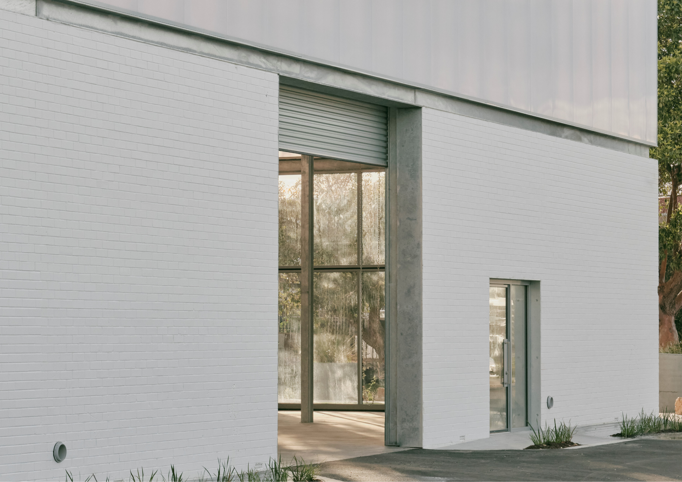 Minimal industrial-style warehouse exterior with white brick walls, translucent upper cladding, and large steel-framed openings.