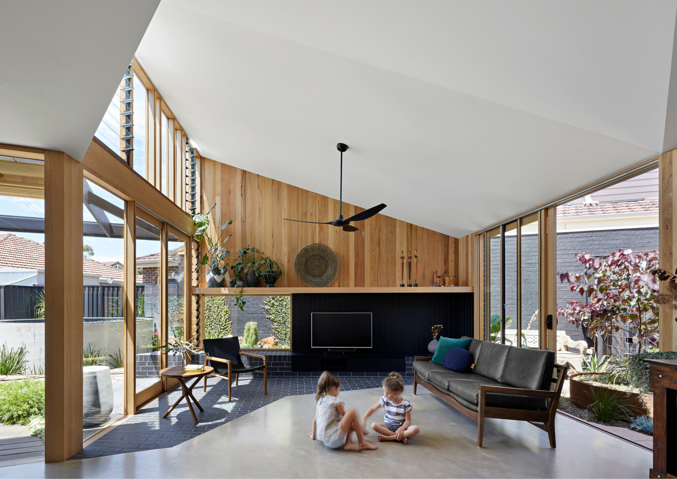 Warm timber-lined living room with large windows and two children sitting on the floor.