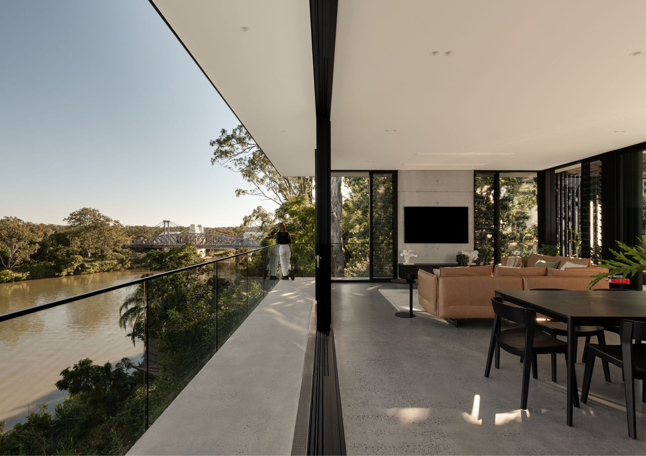 Contemporary riverside living space with polished concrete floors, expansive balcony, and panoramic views across the Brisbane River and bridge.