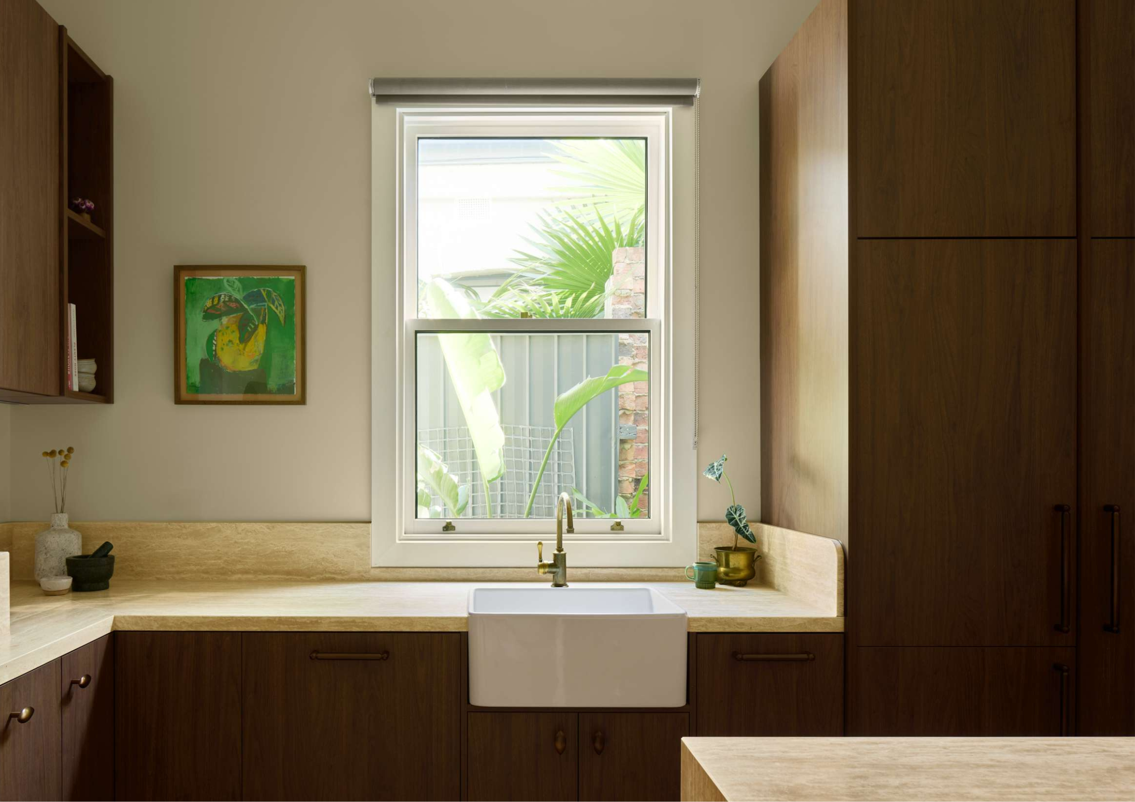 Warm timber kitchen with farmhouse sink, stone benchtops, and soft natural light through a central window.