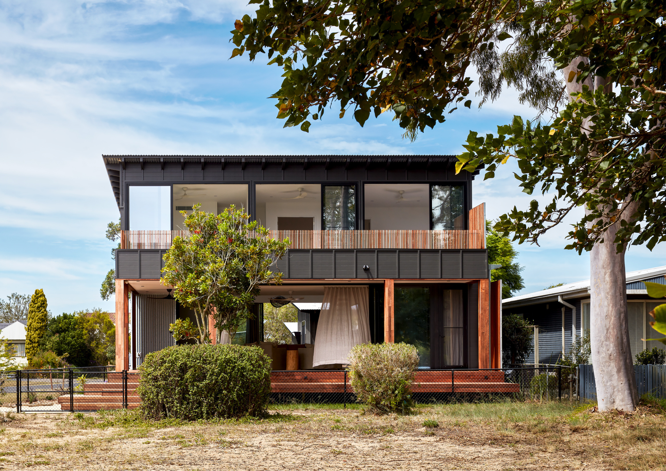 Elevated coastal home with dark cladding, timber accents, and expansive upper-level glazing overlooking a native landscape.
