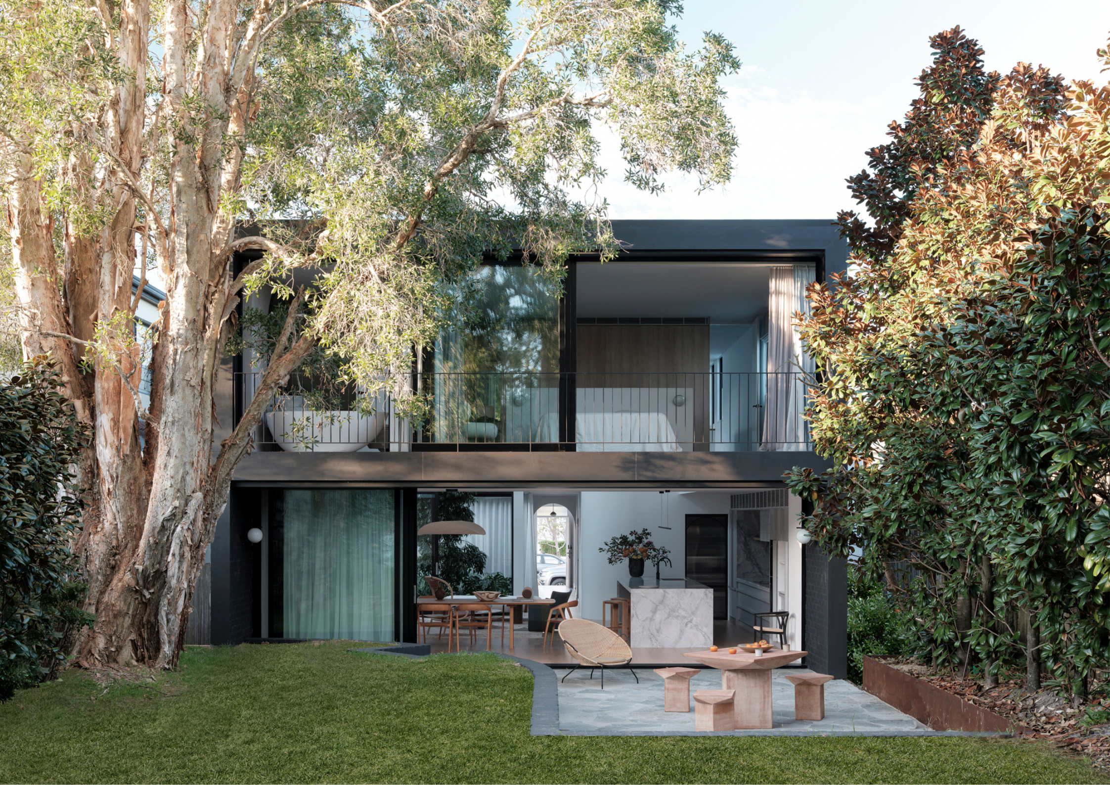 Modern black-clad residence nestled among mature trees, featuring open-plan interiors and large glazed openings to the garden.