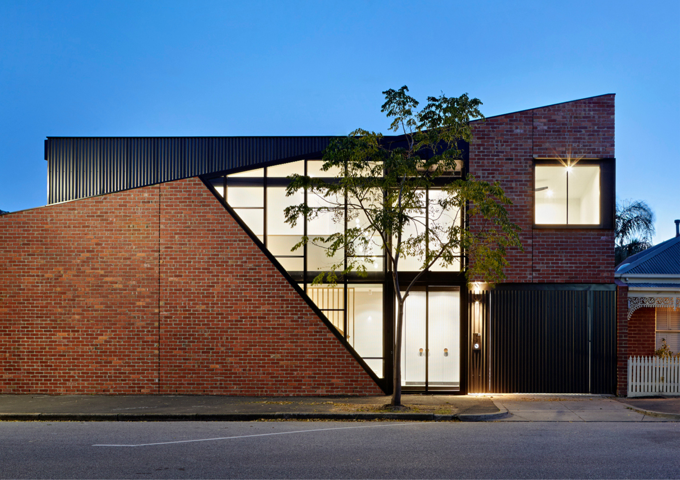 Contemporary brick and black metal house with angular roofline and large glazed façade at dusk.