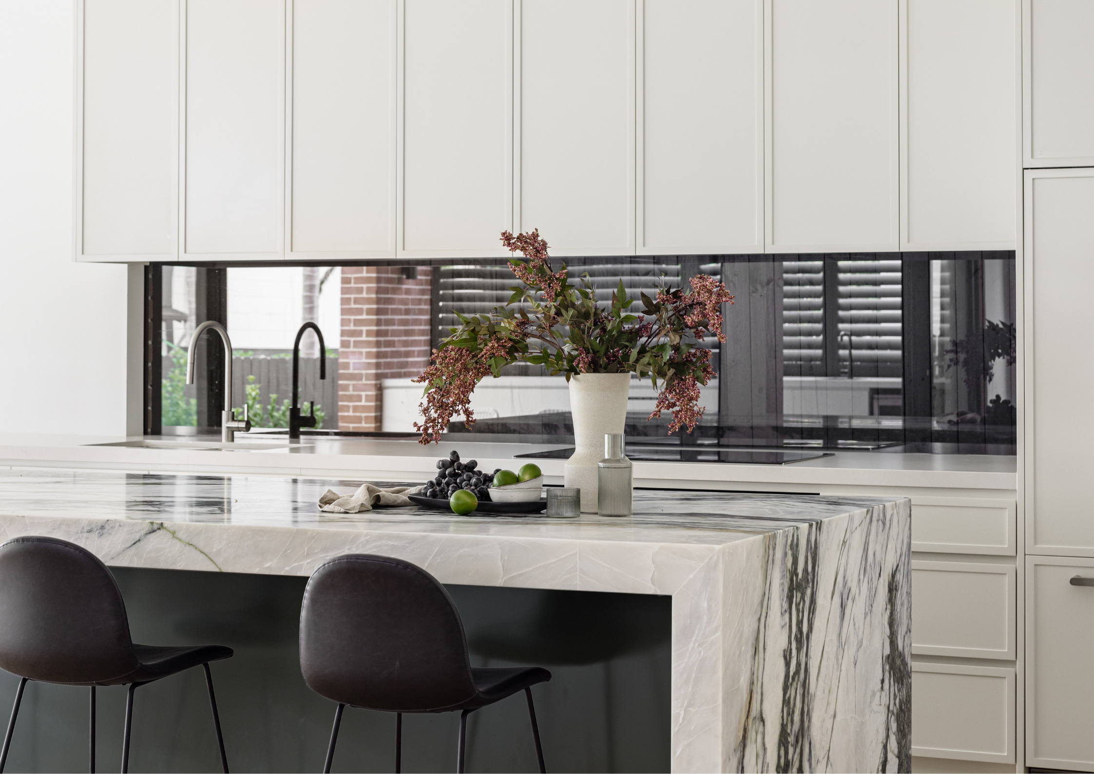 Minimal white kitchen with marble waterfall island, shaker cabinetry, and black-framed splashback window.