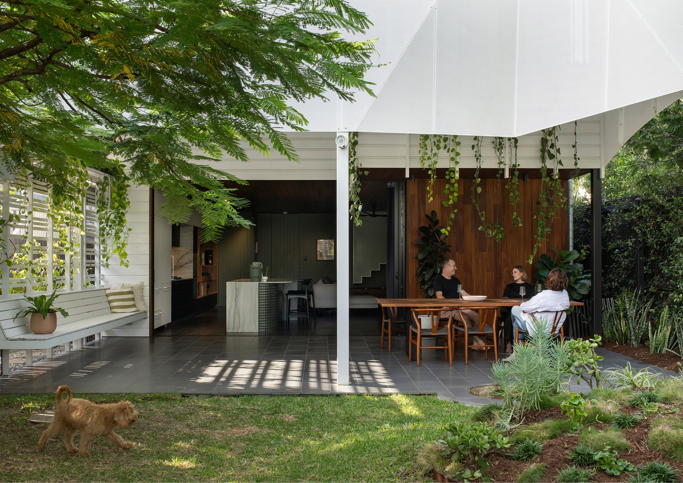 Open-air subtropical entertaining area with hanging greenery, timber dining setting, and seamless indoor-outdoor connection to the garden.