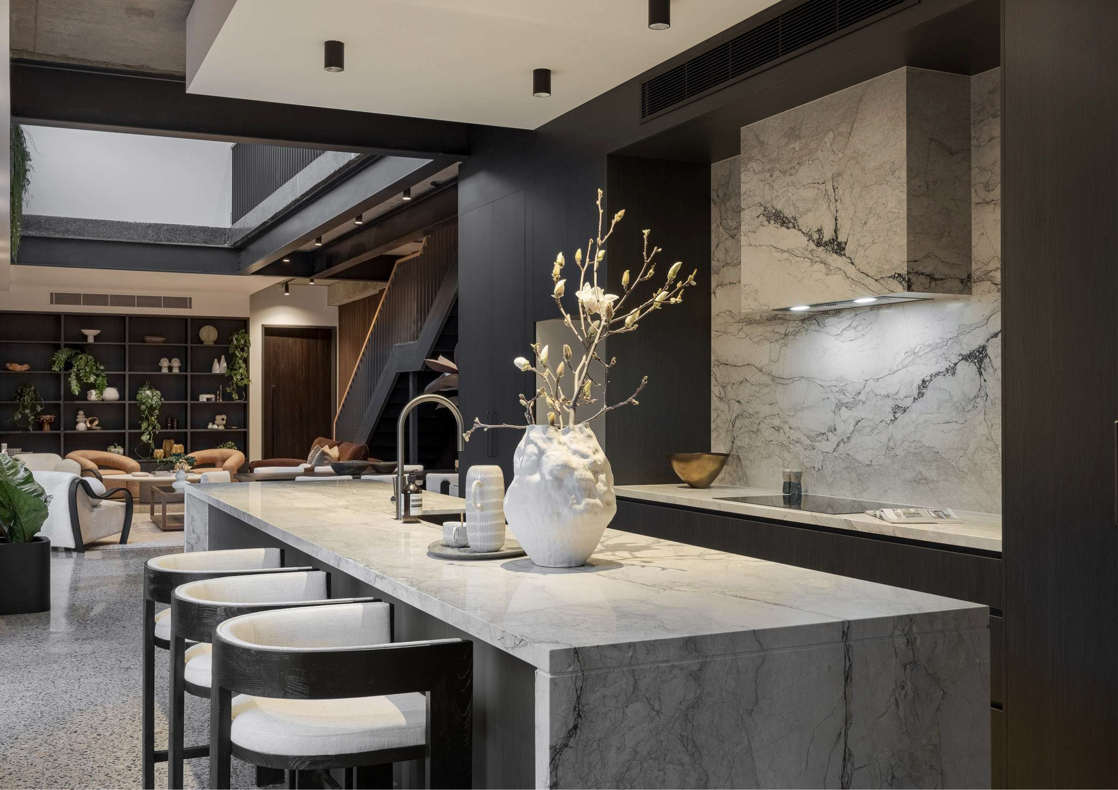 Dark moody kitchen with dramatic marble island, black joinery, and open-plan entertaining space.