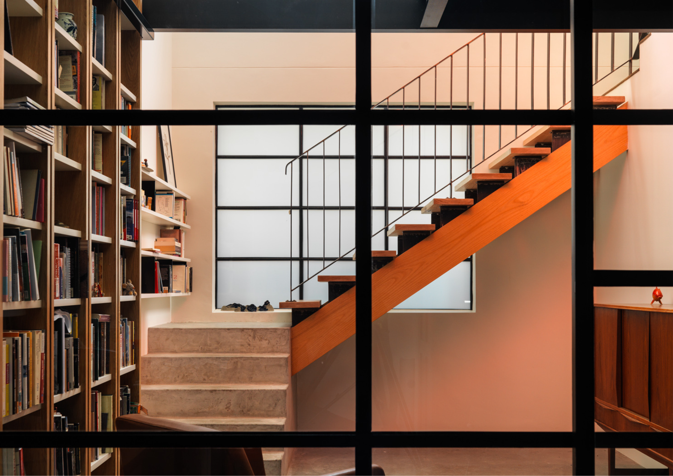 Interior view of staircase with timber steps, black framing, and surrounding bookshelves.