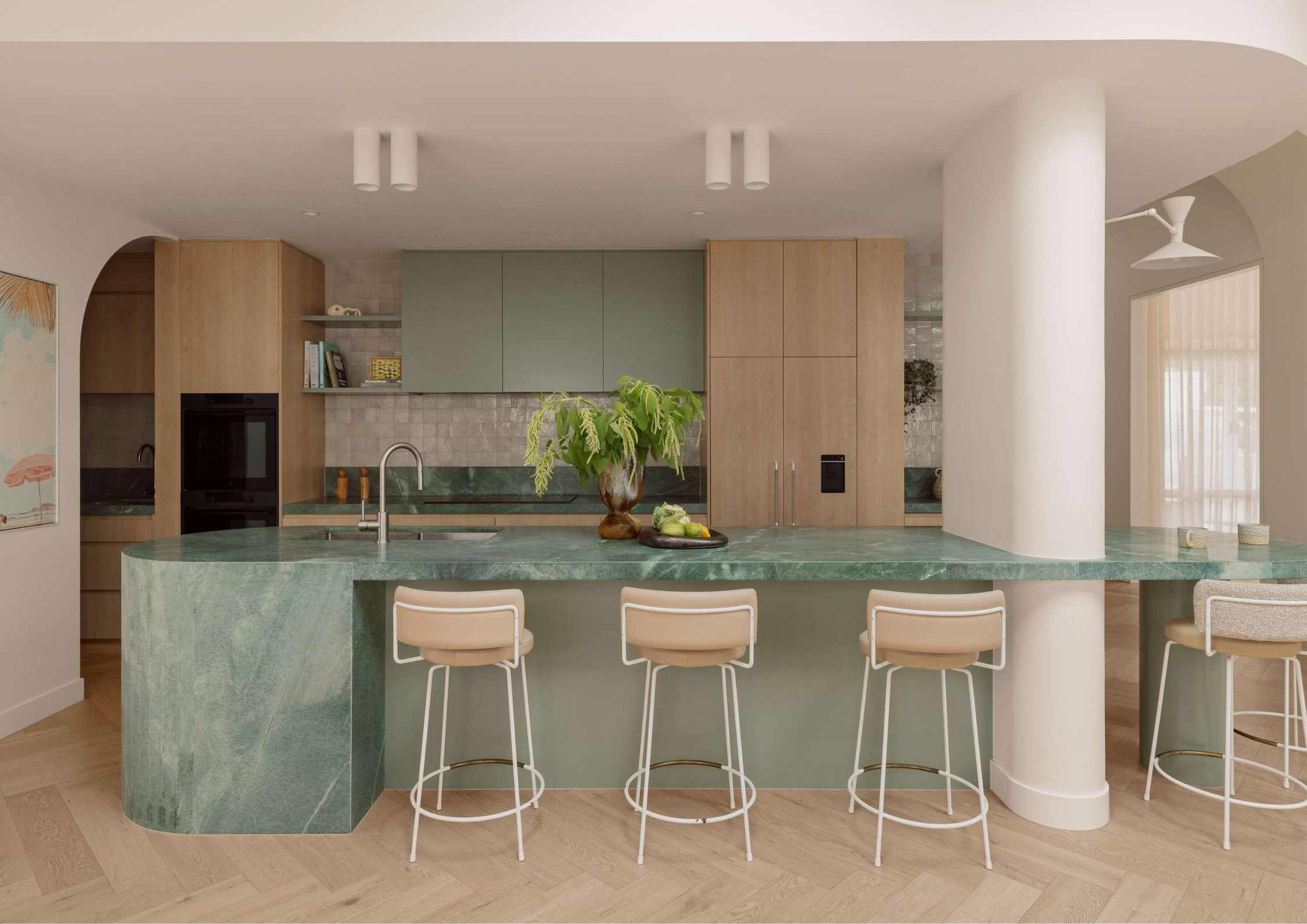 Contemporary green stone kitchen with curved island, timber cabinetry, and soft neutral palette.