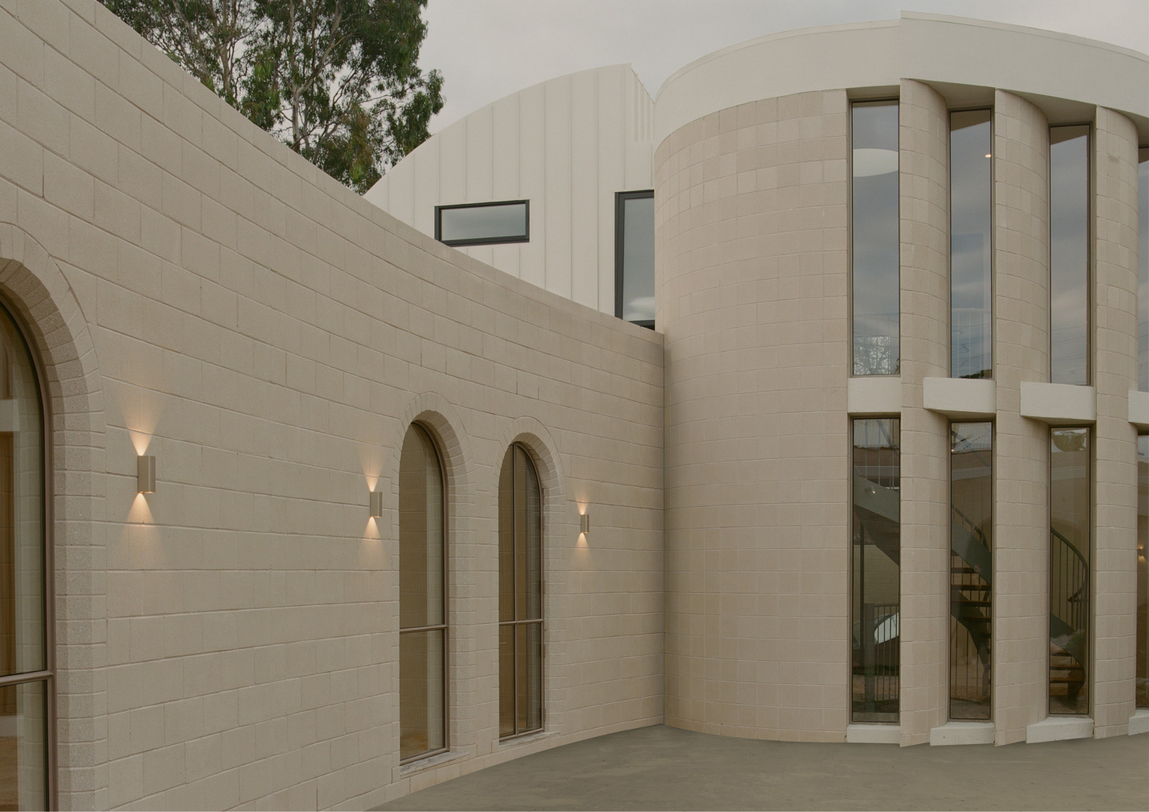 Curved pale brick building with arched windows and soft exterior lighting.