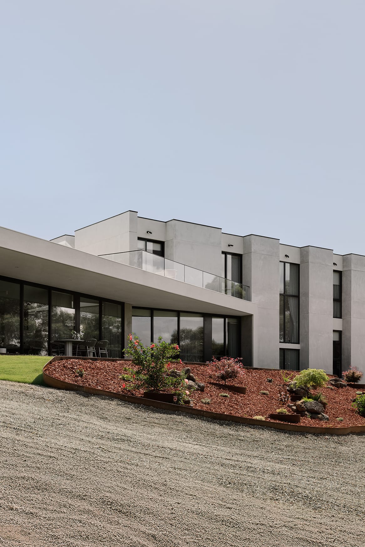 Large contemporary hillside residence with expansive glazing, concrete finishes and landscaped gardens overlooking a sloped site.