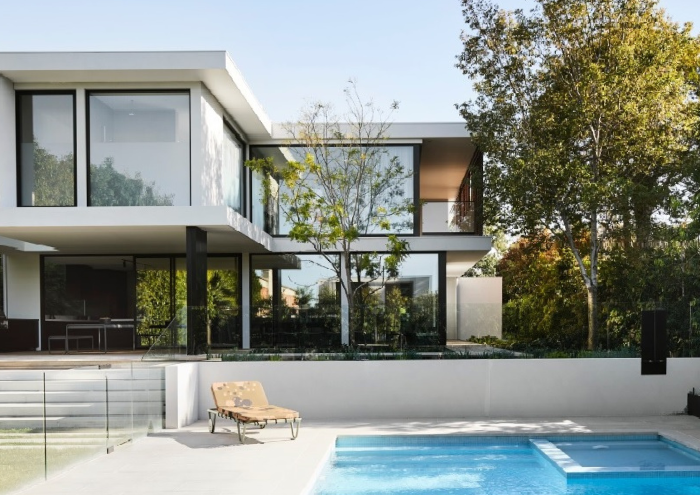 Modern two-storey white house with large glass windows overlooking a pool and landscaped garden.