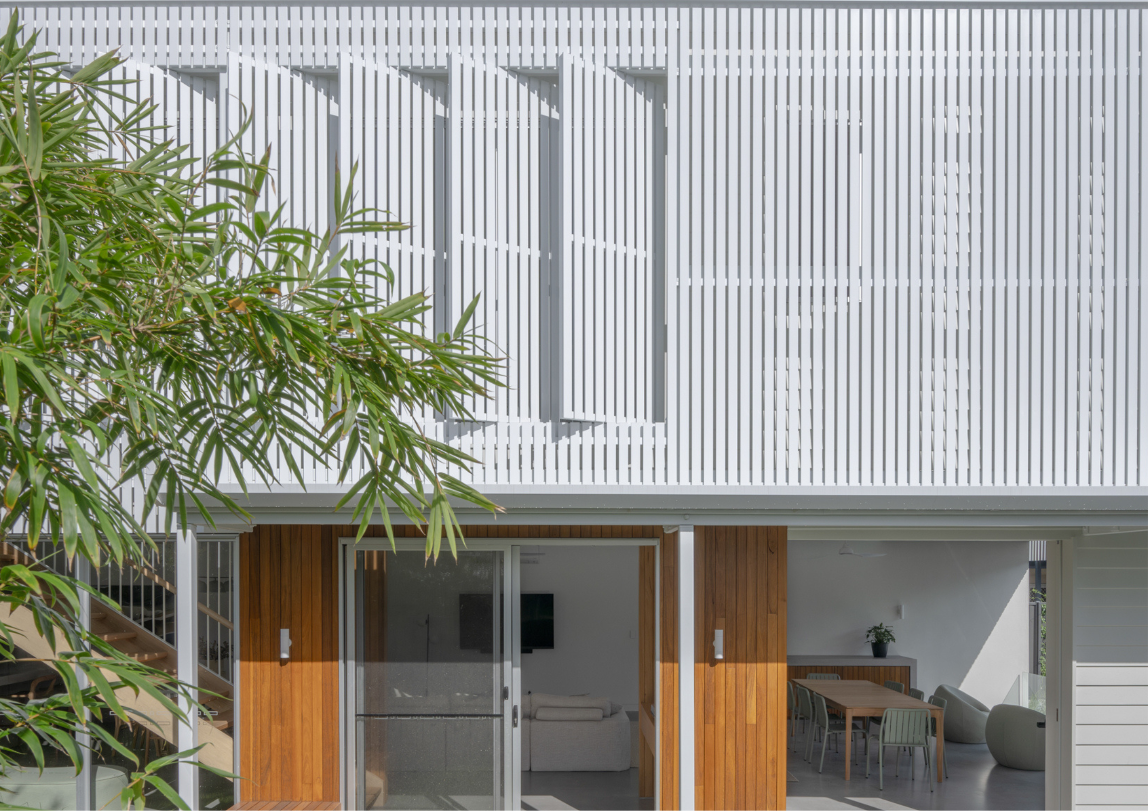 Light-filled home with white vertical slatted façade and timber accents opening to a dining space.