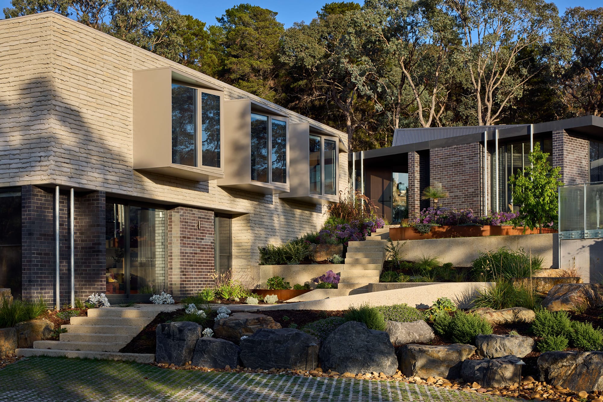 Contemporary brick and timber home set within terraced native landscaping on a sloping bushland site.