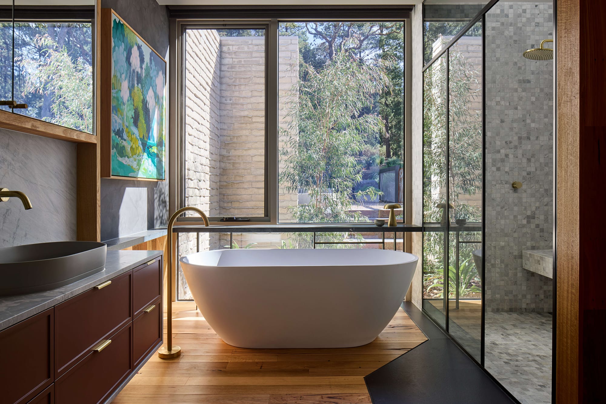 Contemporary bathroom with freestanding bath, timber cabinetry and floor-to-ceiling glazing overlooking landscaped gardens.
