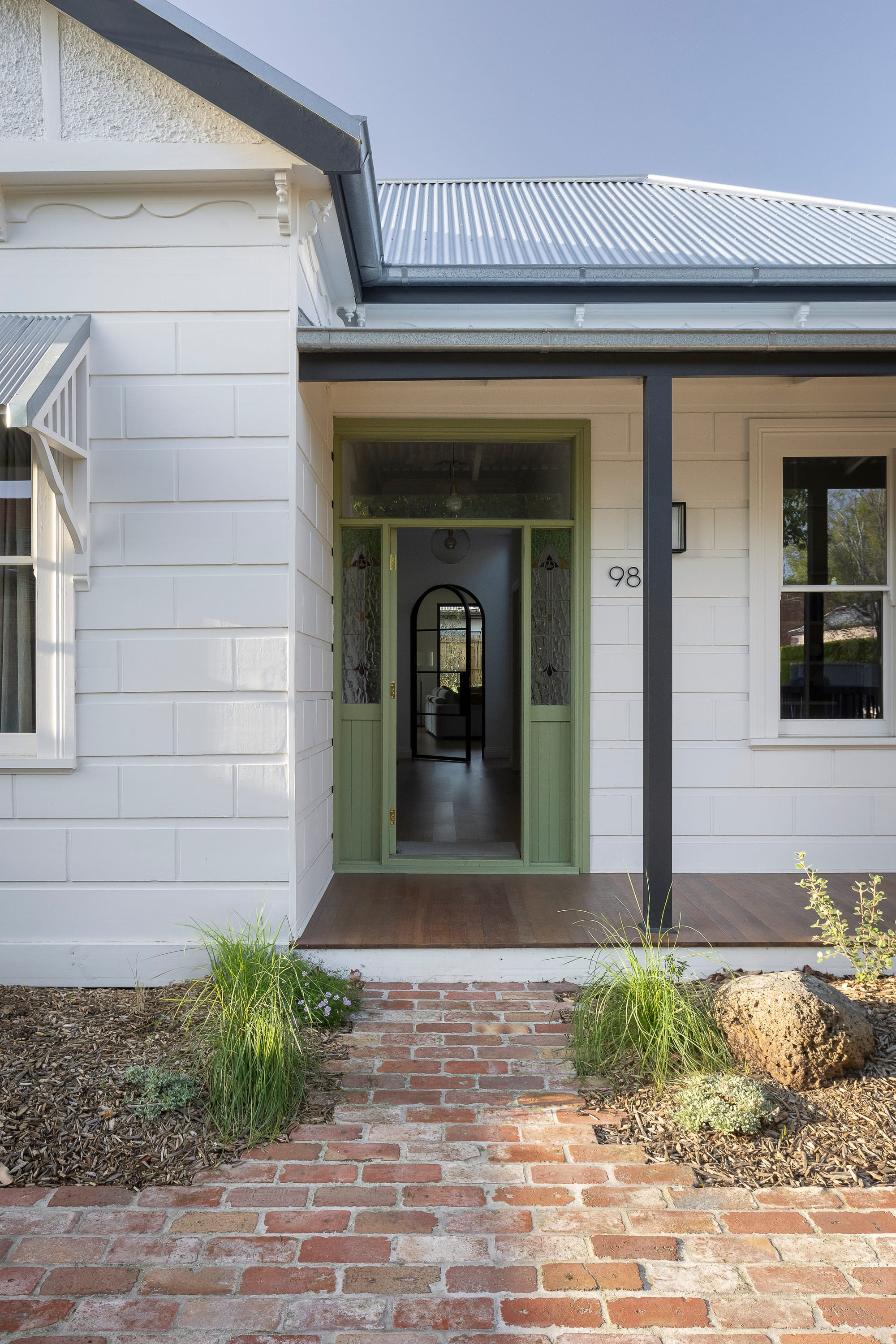 Restored heritage weatherboard home with a mint green entry door, brick pathway, and landscaped front garden.