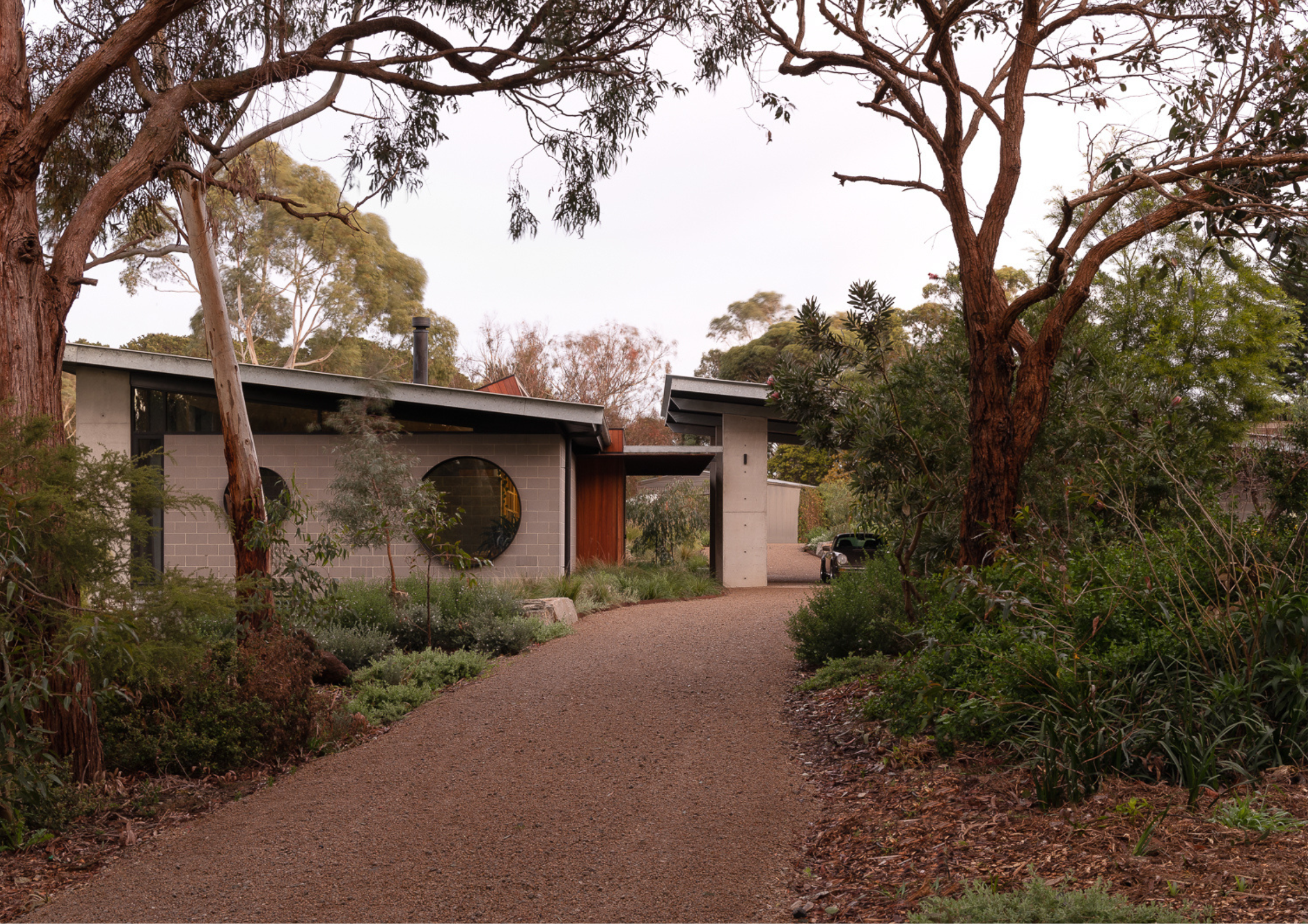 Contemporary home set in native bushland with a gravel driveway and circular window feature.