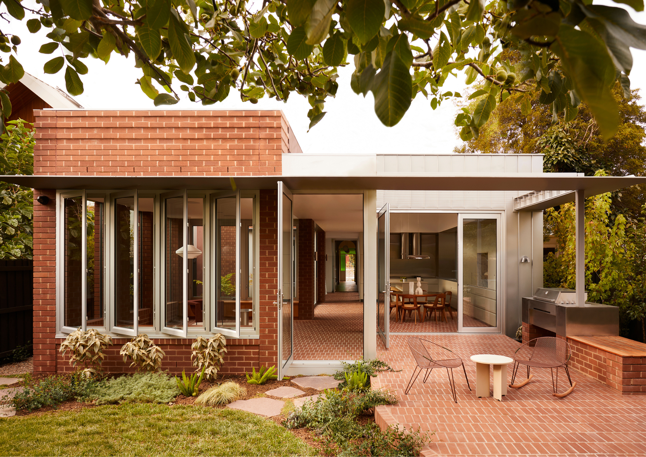 Single-storey brick house with folding glass doors opening to a courtyard and garden.