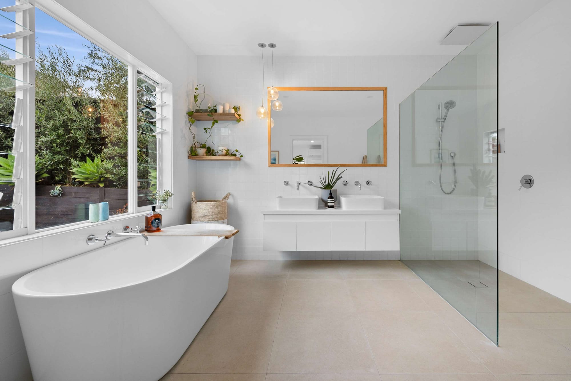 Bright contemporary bathroom with freestanding bath, floating double vanity and large window framing lush greenery.