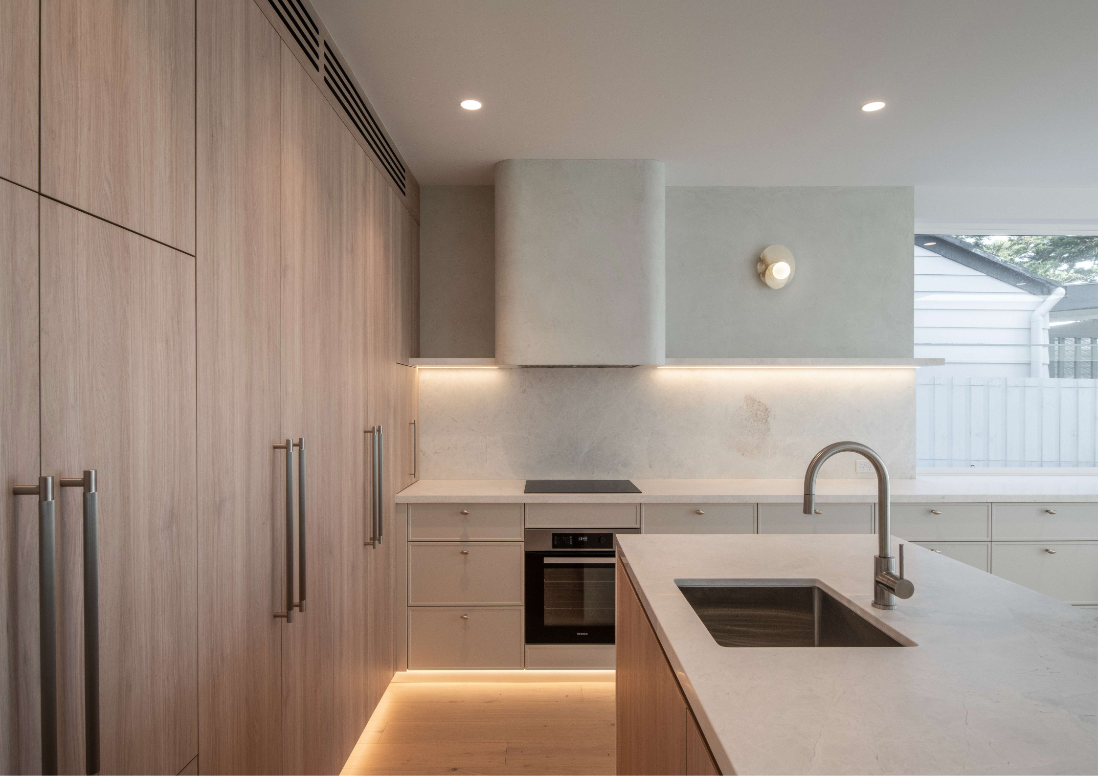 Soft neutral kitchen with timber veneer cabinetry, stone island, and concealed rangehood lighting.