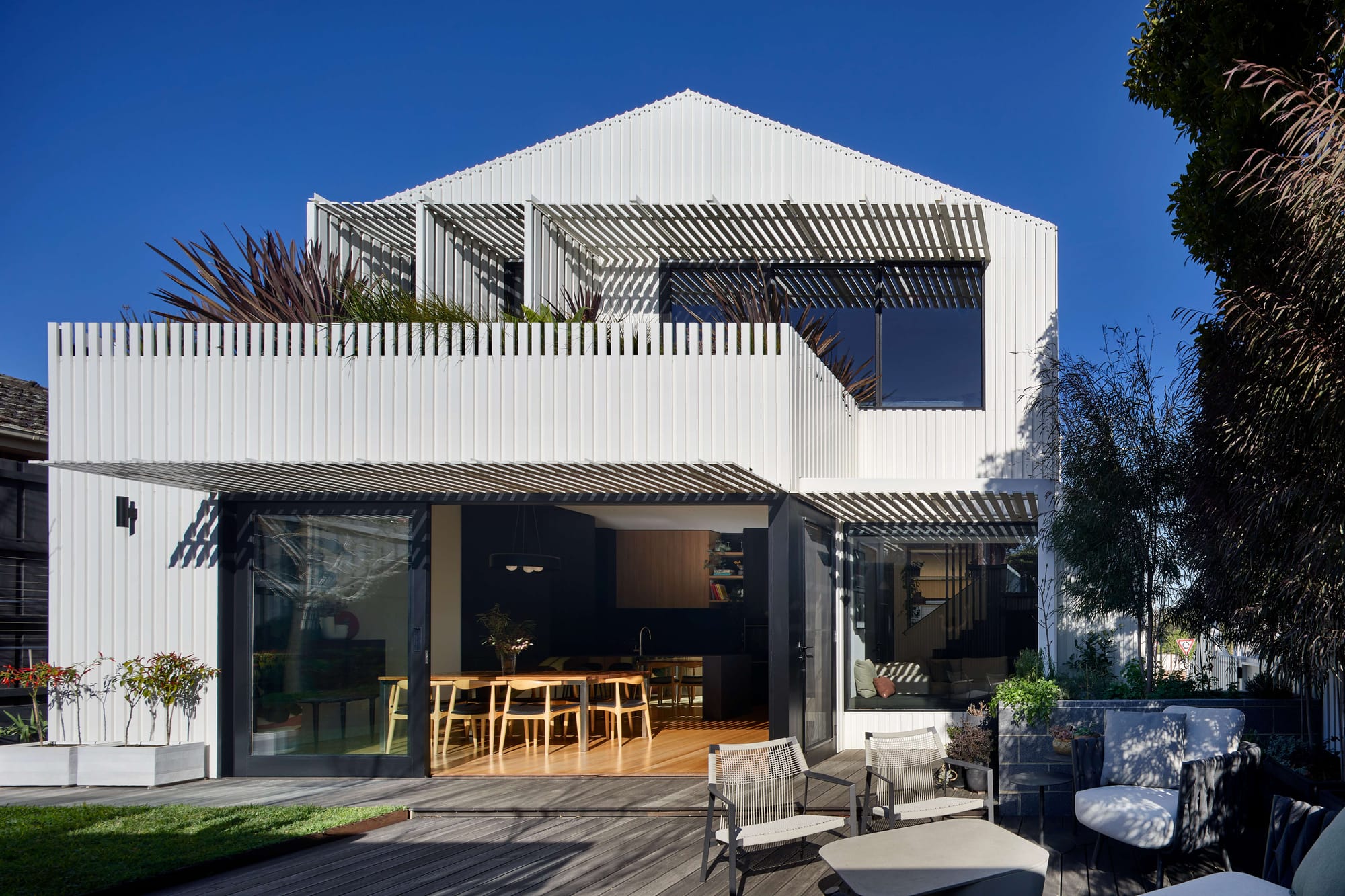 Modern white gabled home with louvred screening, expansive glazing, and outdoor entertaining terrace opening onto a landscaped courtyard.