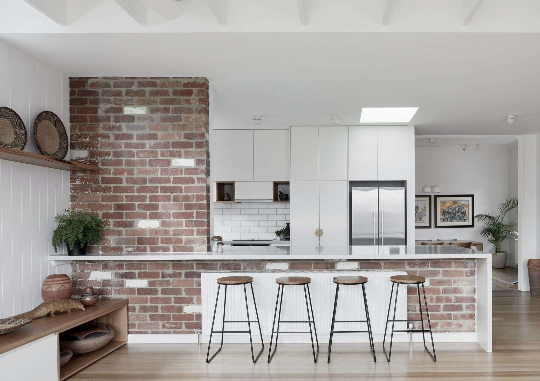 Bright white kitchen framed by exposed brick, integrated island seating, and minimalist cabinetry.