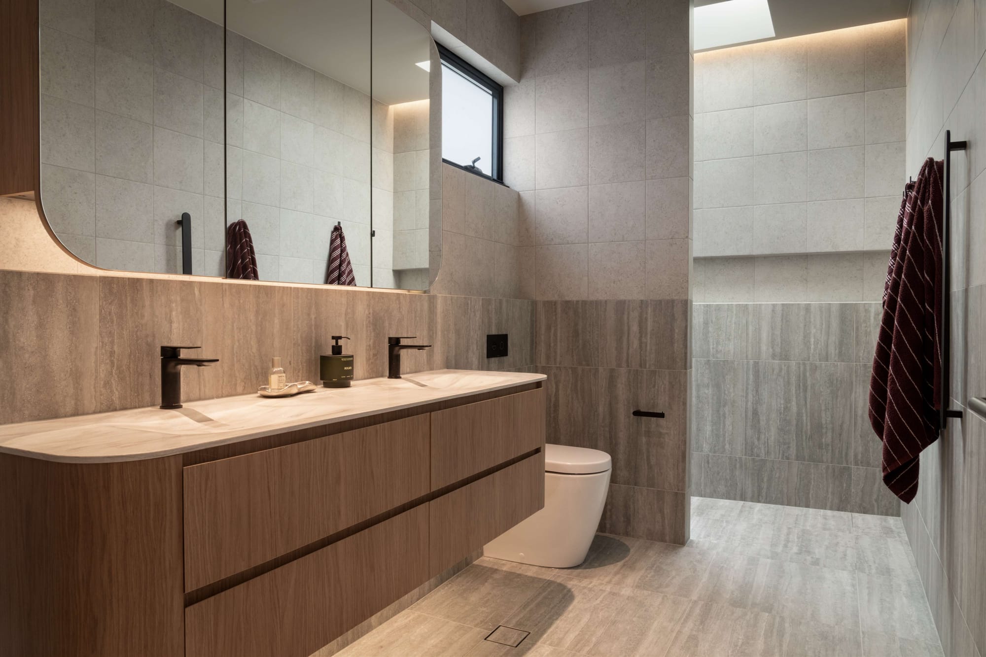 Contemporary bathroom with freestanding bath, timber cabinetry and floor-to-ceiling glazing overlooking landscaped gardens.